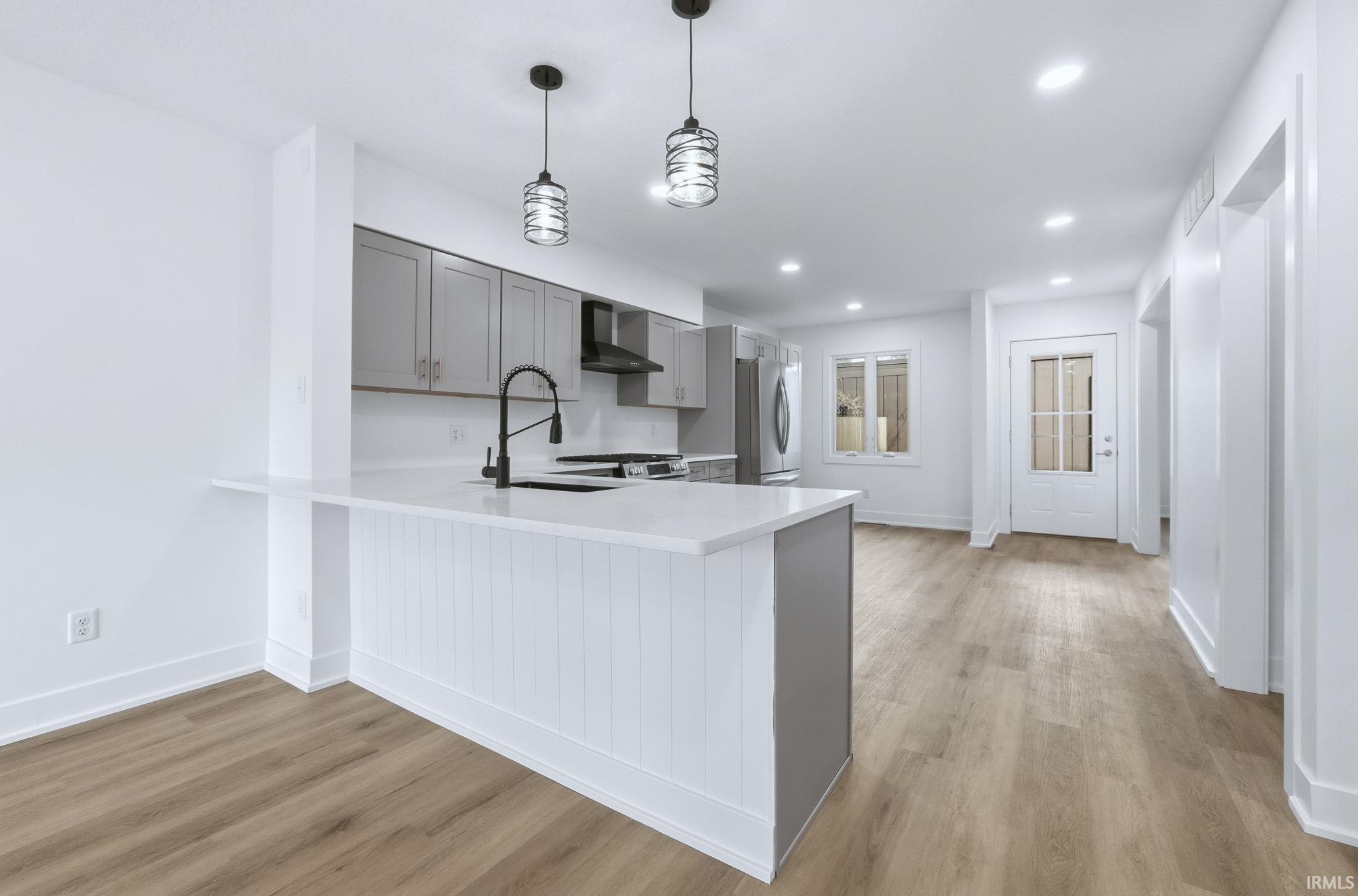 Kitchen featuring gray cabinets, a peninsula, decorative light fixtures, light wood-type flooring, and recessed lighting