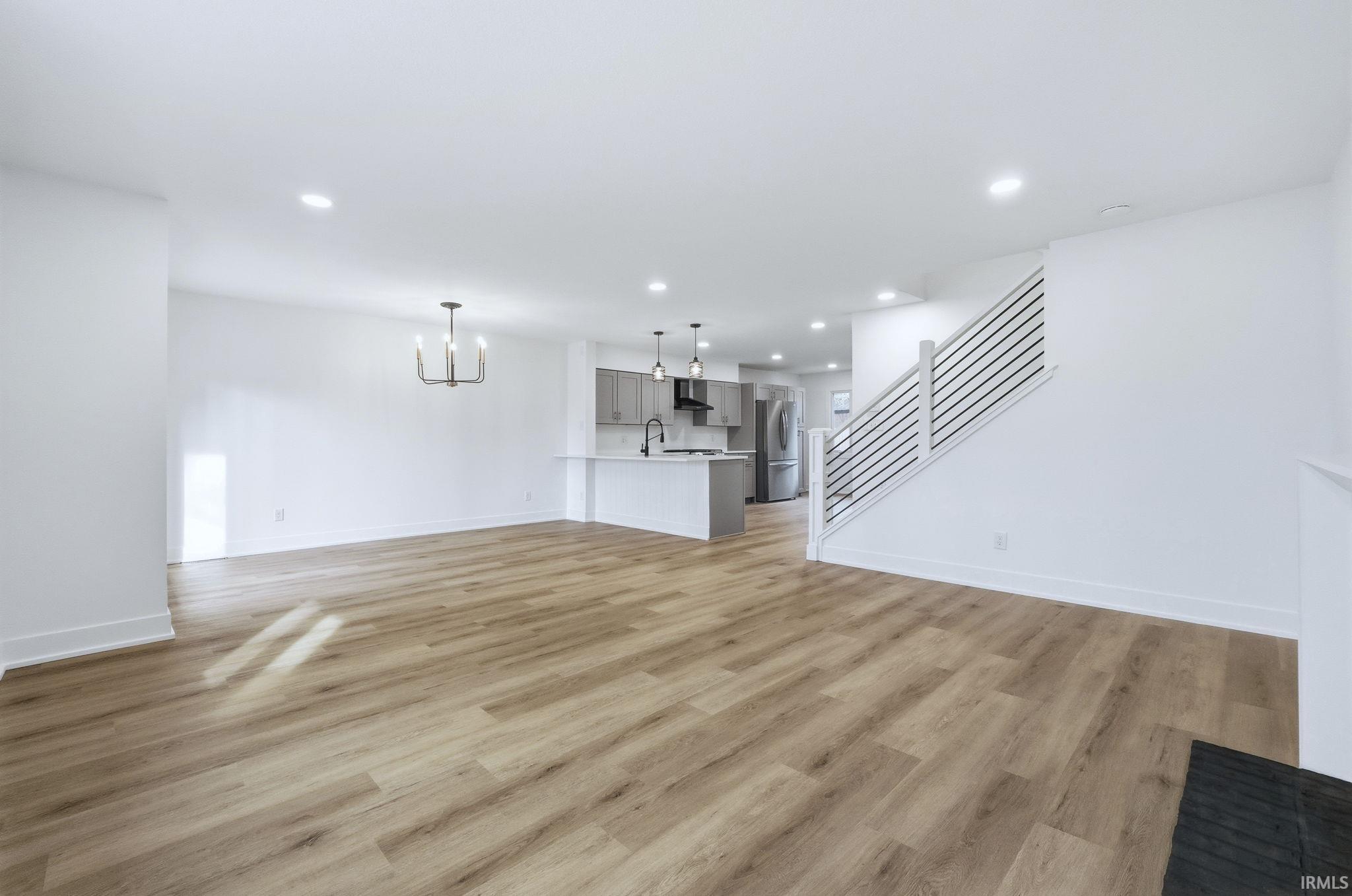 Unfurnished living room with stairway, a chandelier, recessed lighting, and light wood-style floors
