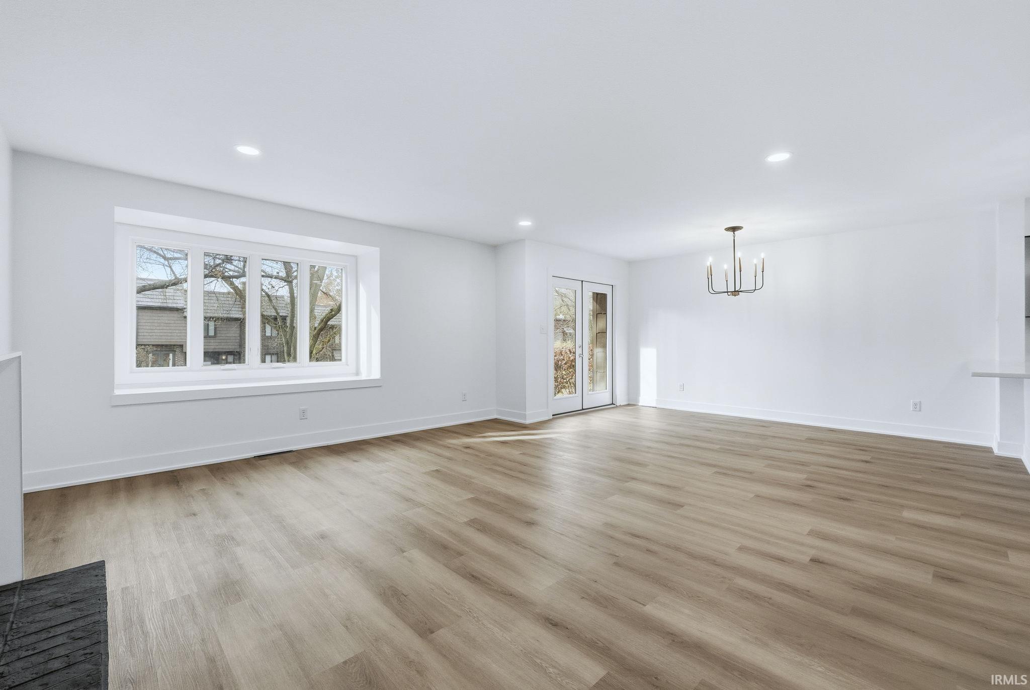 Unfurnished living room featuring plenty of natural light, light wood finished floors, recessed lighting, and a chandelier
