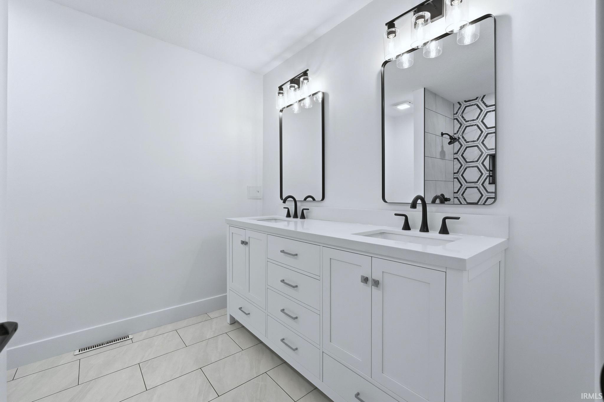 Full bathroom featuring double vanity, light tile patterned flooring, and tiled shower