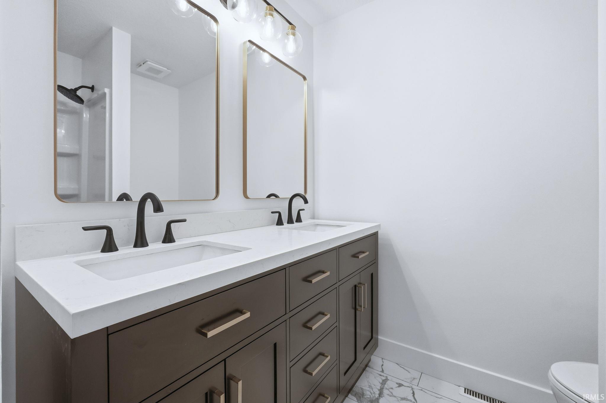 Full bathroom featuring light marble finish floors, double vanity, and a shower