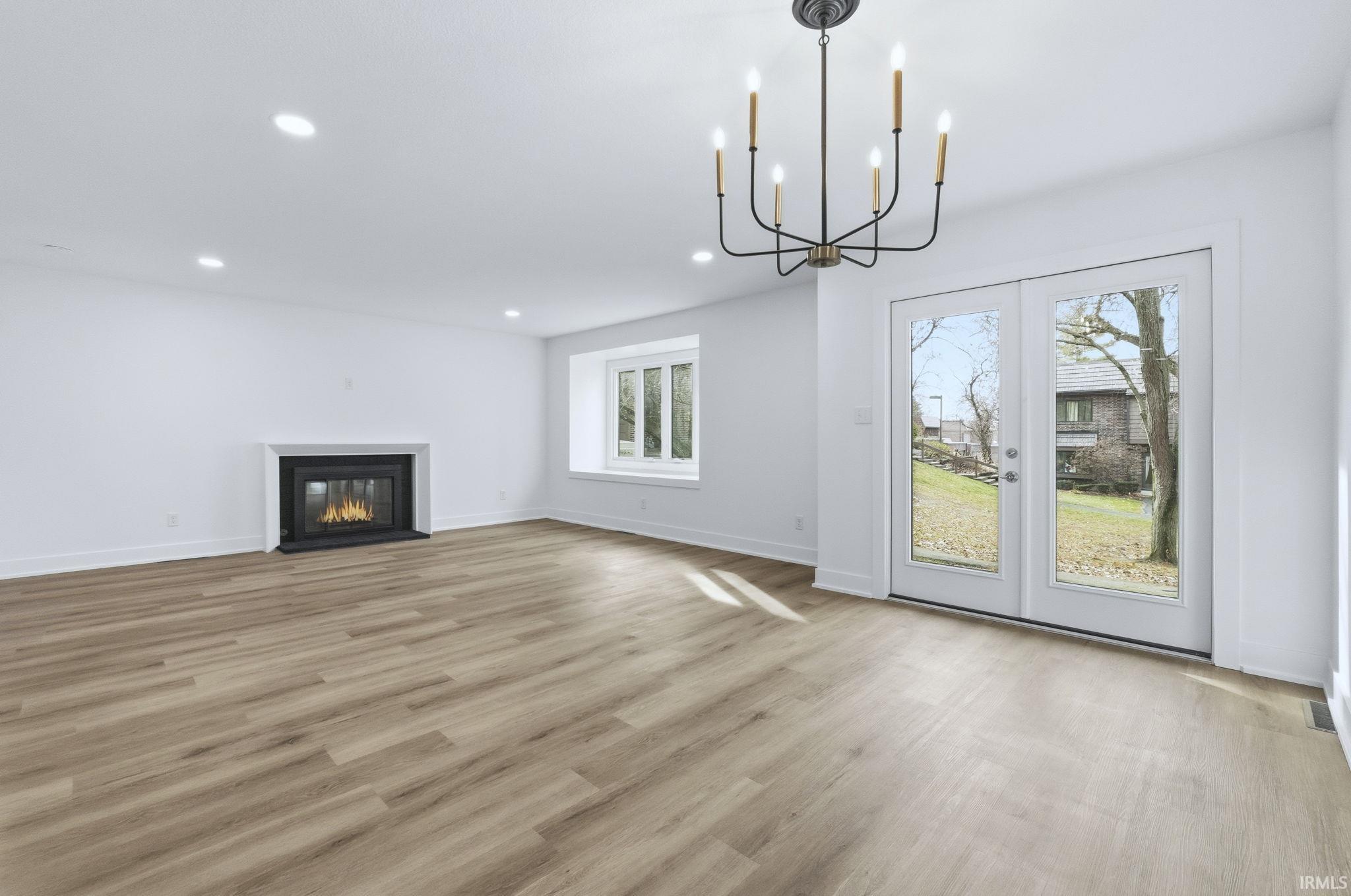 Unfurnished living room with a fireplace with flush hearth, french doors, light wood-style floors, a chandelier, and recessed lighting