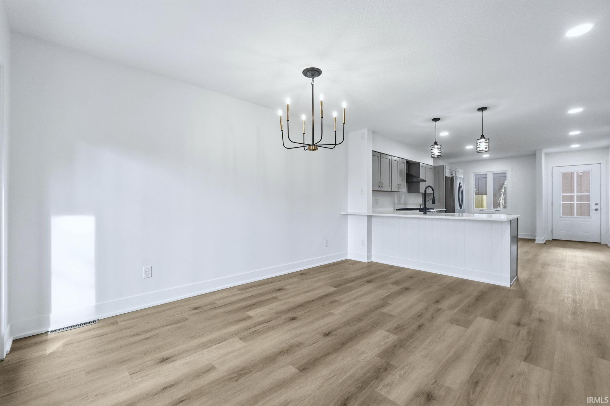 Kitchen with gray cabinets, pendant lighting, a chandelier, a peninsula, and light wood-style floors