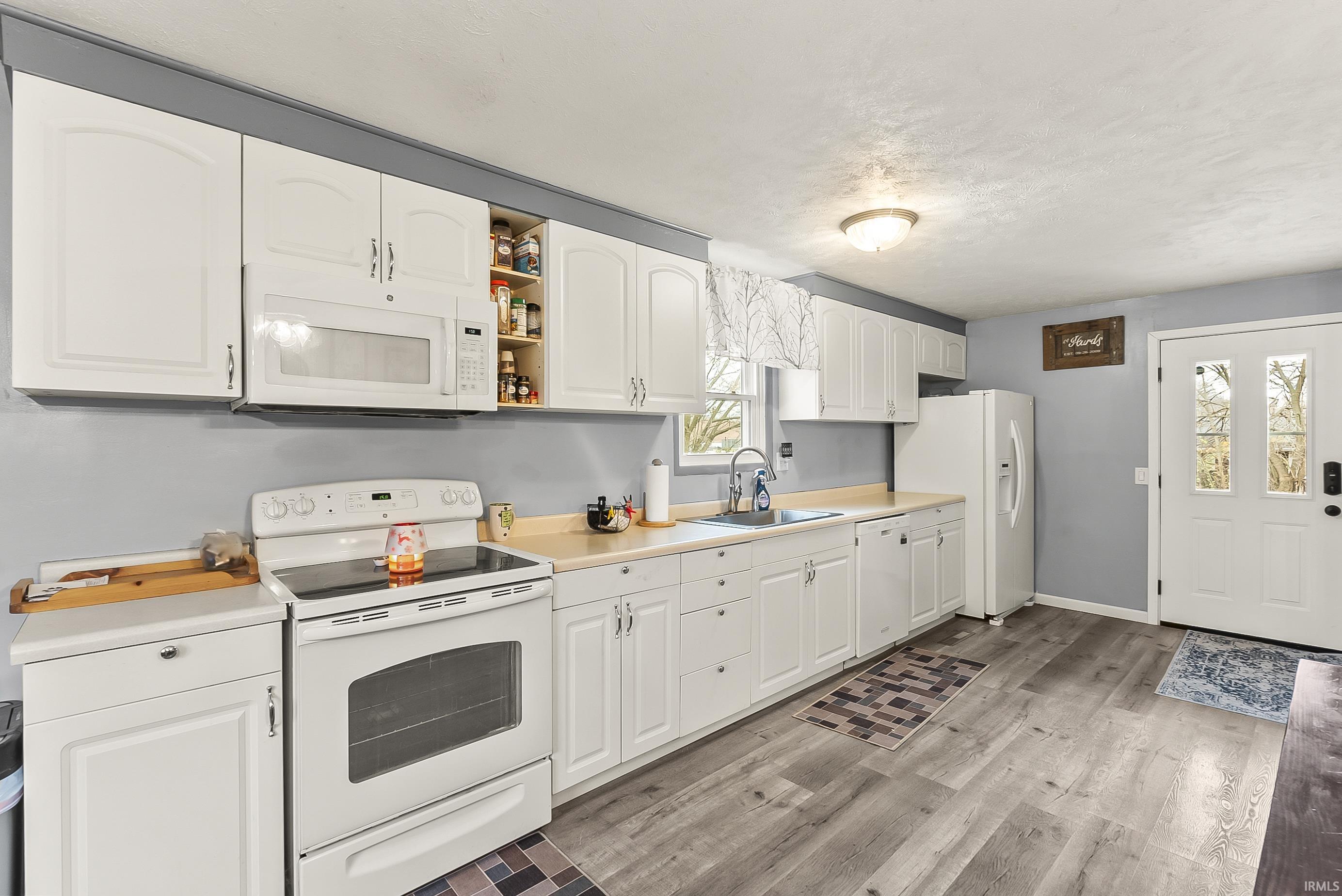 Kitchen with white appliances, white cabinets, light countertops, open shelves, and light wood-style flooring