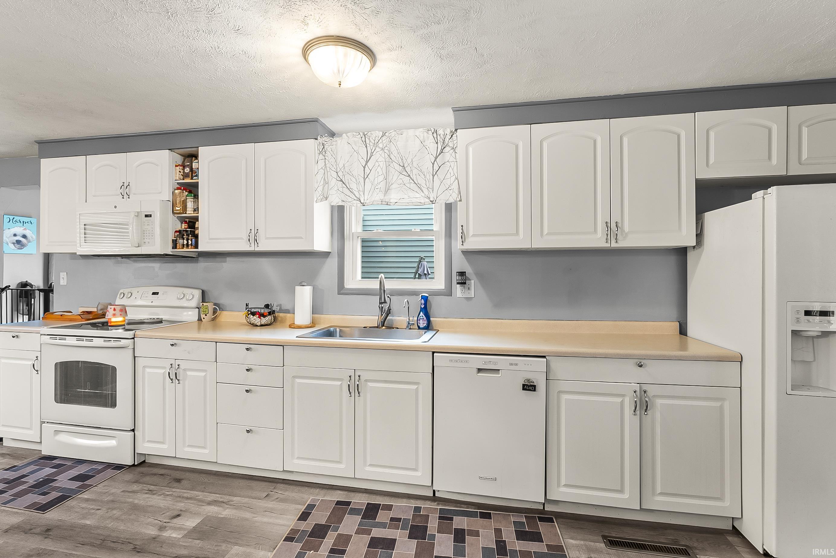 Kitchen featuring white appliances, white cabinets, light countertops, wood finished floors, and a textured ceiling