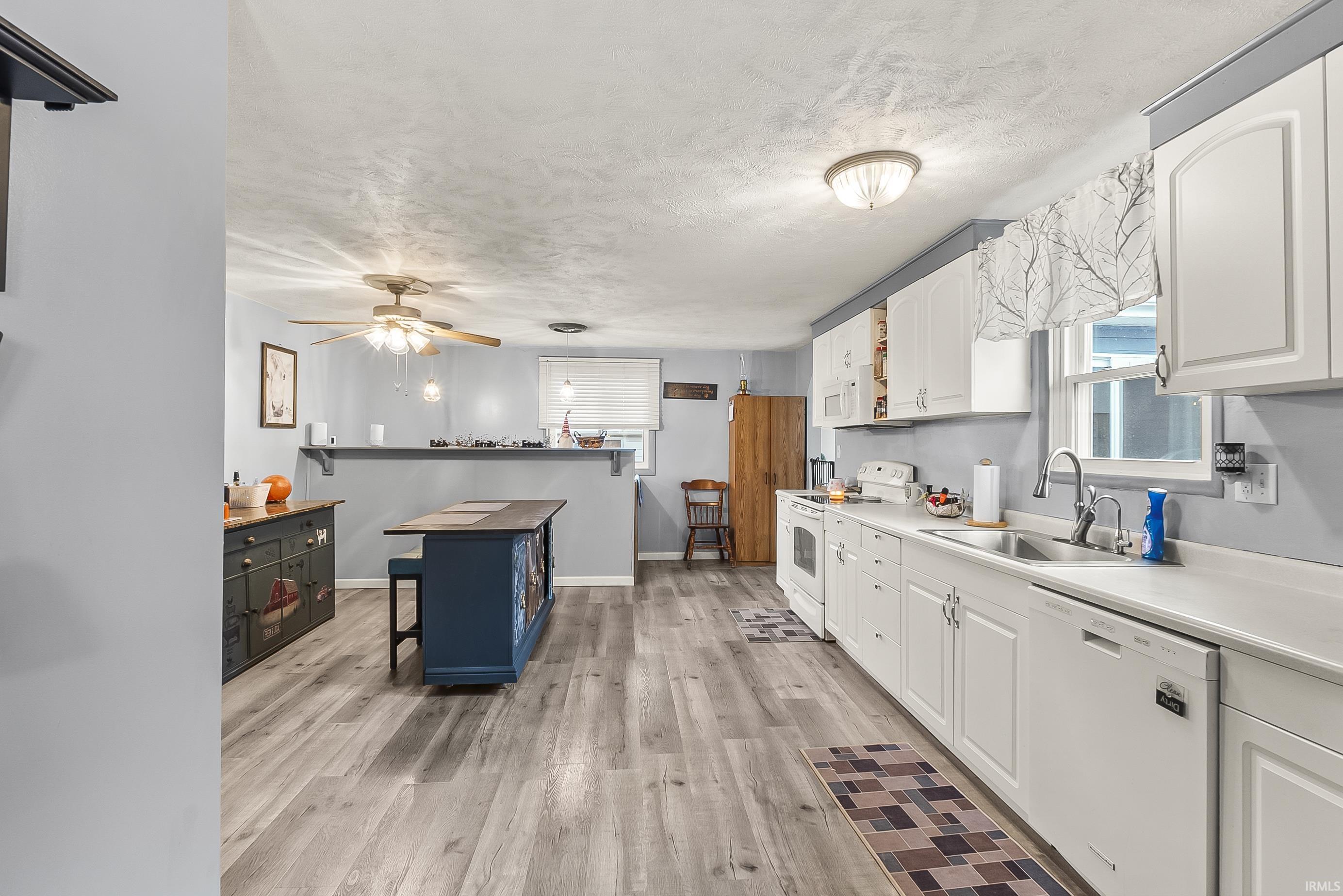 Kitchen with white appliances, a kitchen breakfast bar, white cabinetry, light wood finished floors, and a textured ceiling