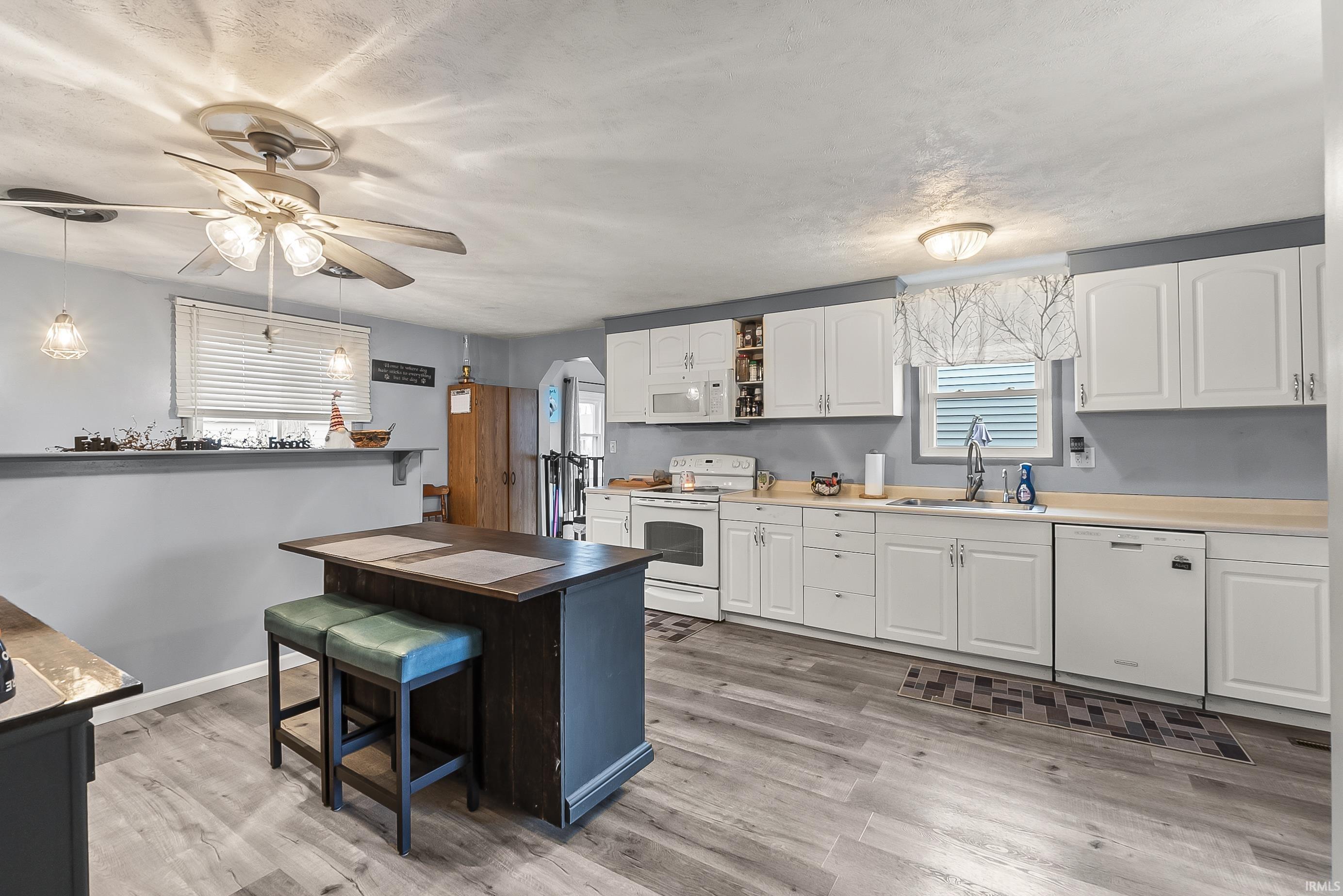 Kitchen featuring a breakfast bar area, white cabinets, white appliances, and light wood-style flooring