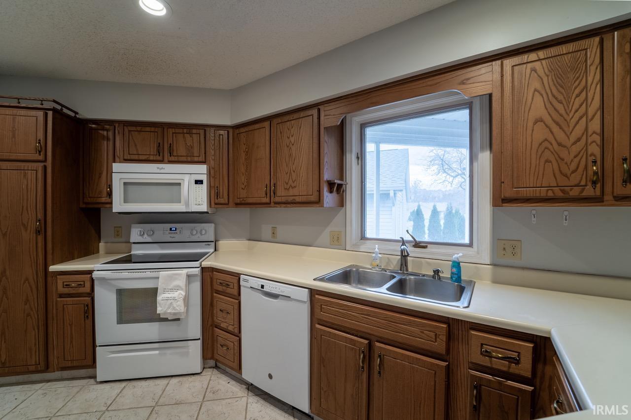 Kitchen with white appliances, light countertops, brown cabinets, a textured ceiling, and light tile patterned flooring