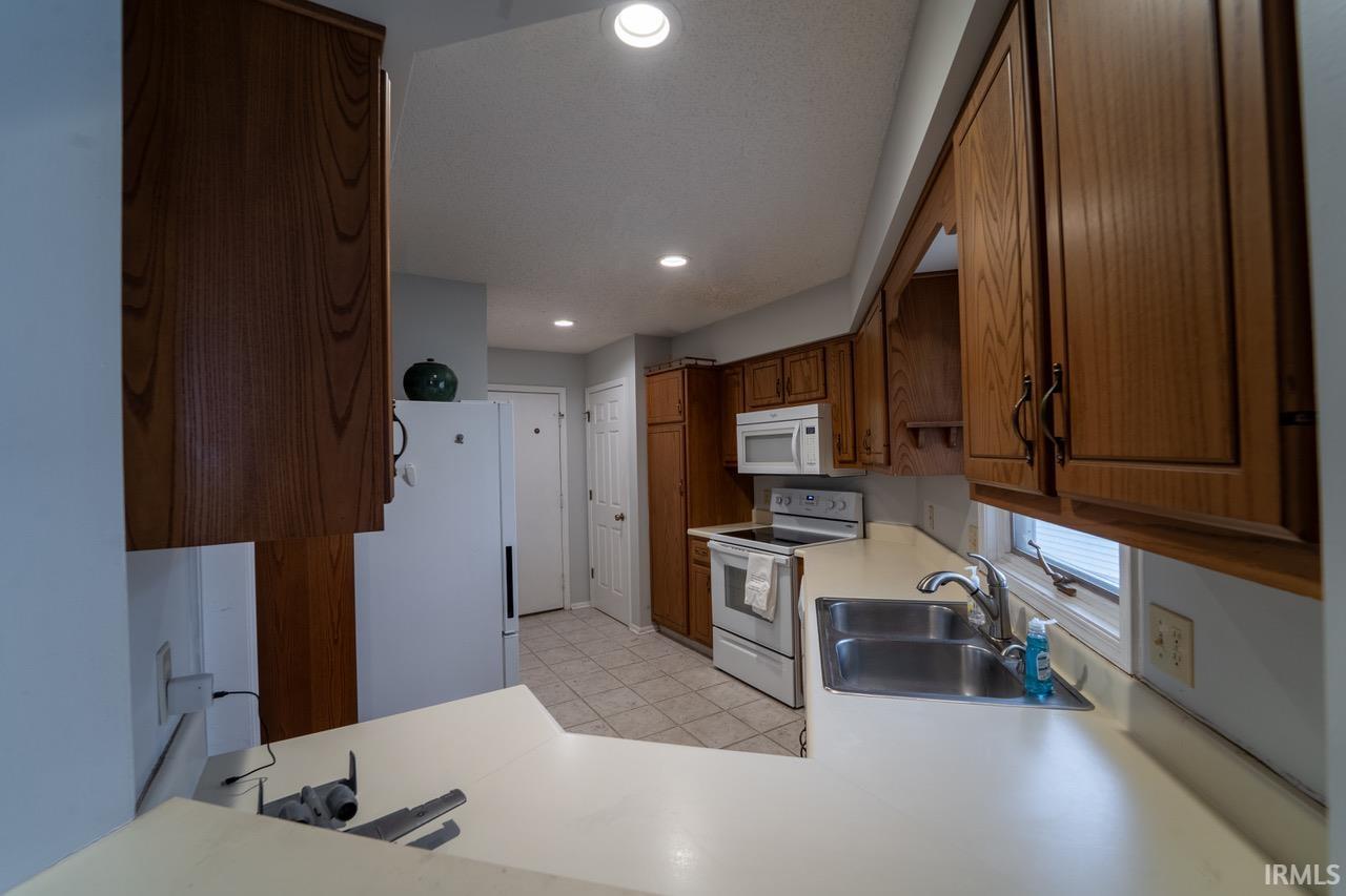 Kitchen with white appliances, light countertops, brown cabinetry, and recessed lighting