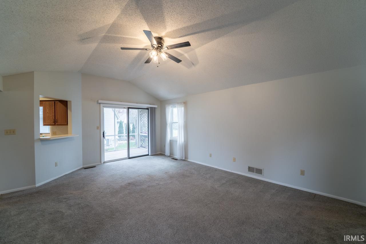 Unfurnished living room featuring ceiling fan, vaulted ceiling, carpet flooring, and a textured ceiling
