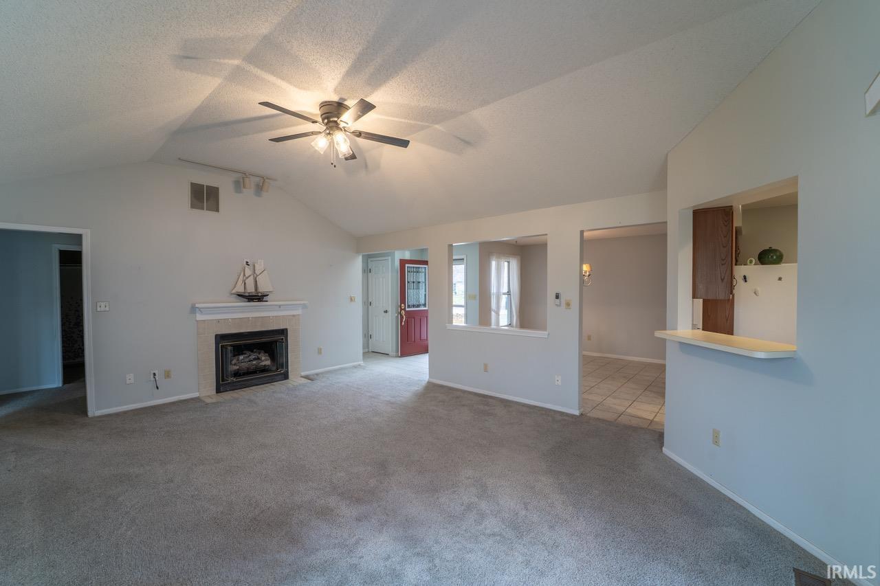 Unfurnished living room featuring a tiled fireplace, carpet flooring, lofted ceiling, ceiling fan, and a textured ceiling