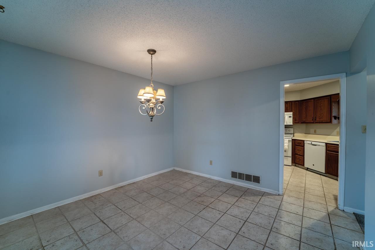 Unfurnished room with a chandelier, a textured ceiling, and light tile patterned flooring