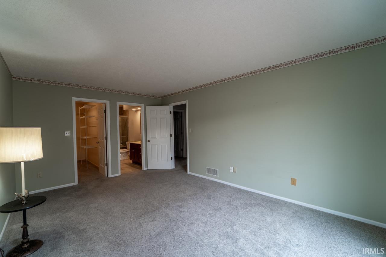 Unfurnished bedroom with a spacious closet, carpet floors, and ensuite bath