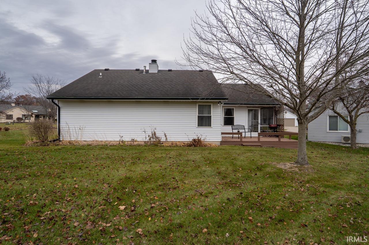 Back of house with a lawn, a deck, roof with shingles, and a chimney