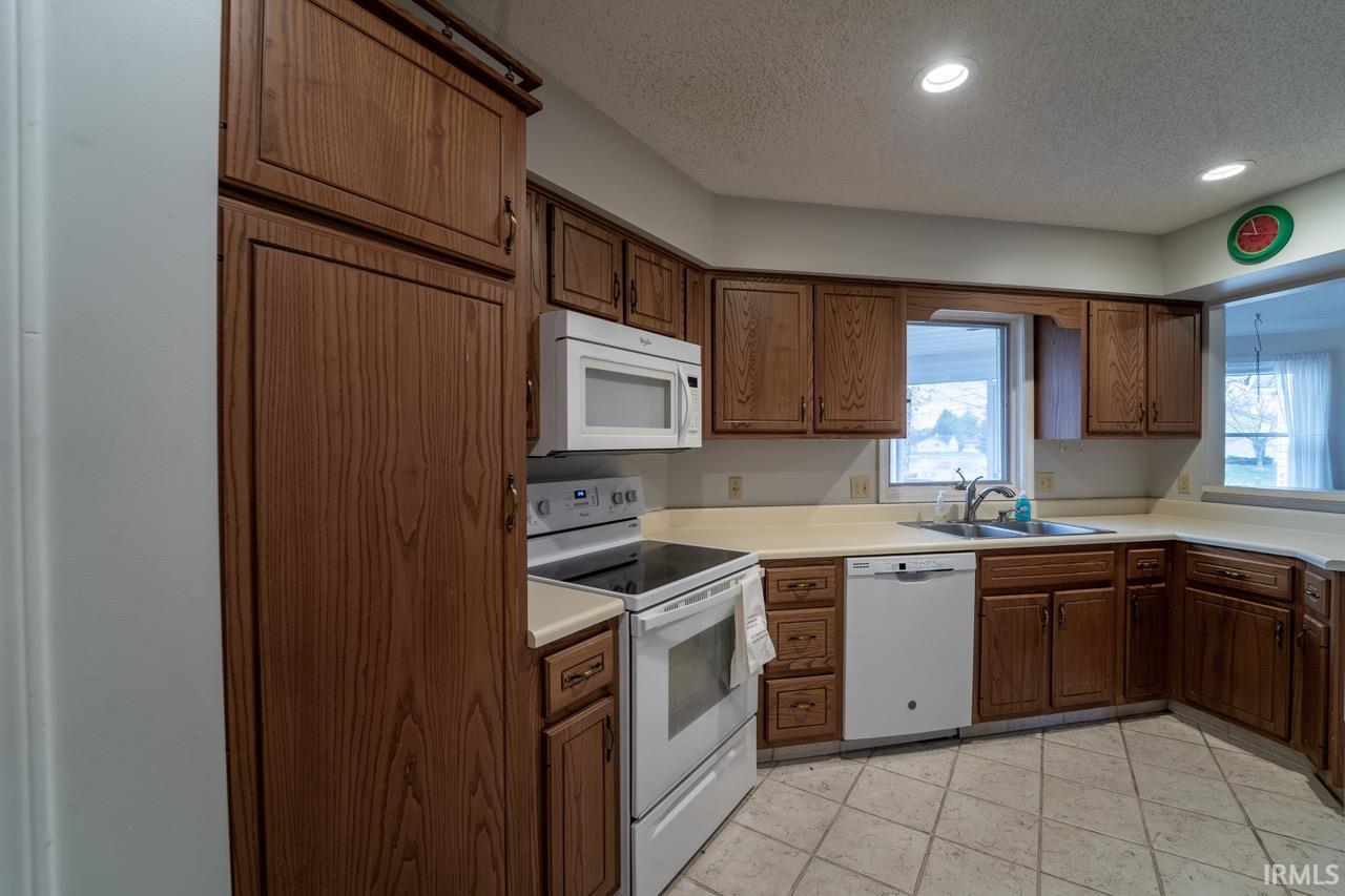 Kitchen featuring white appliances, a textured ceiling, recessed lighting, light countertops, and brown cabinetry