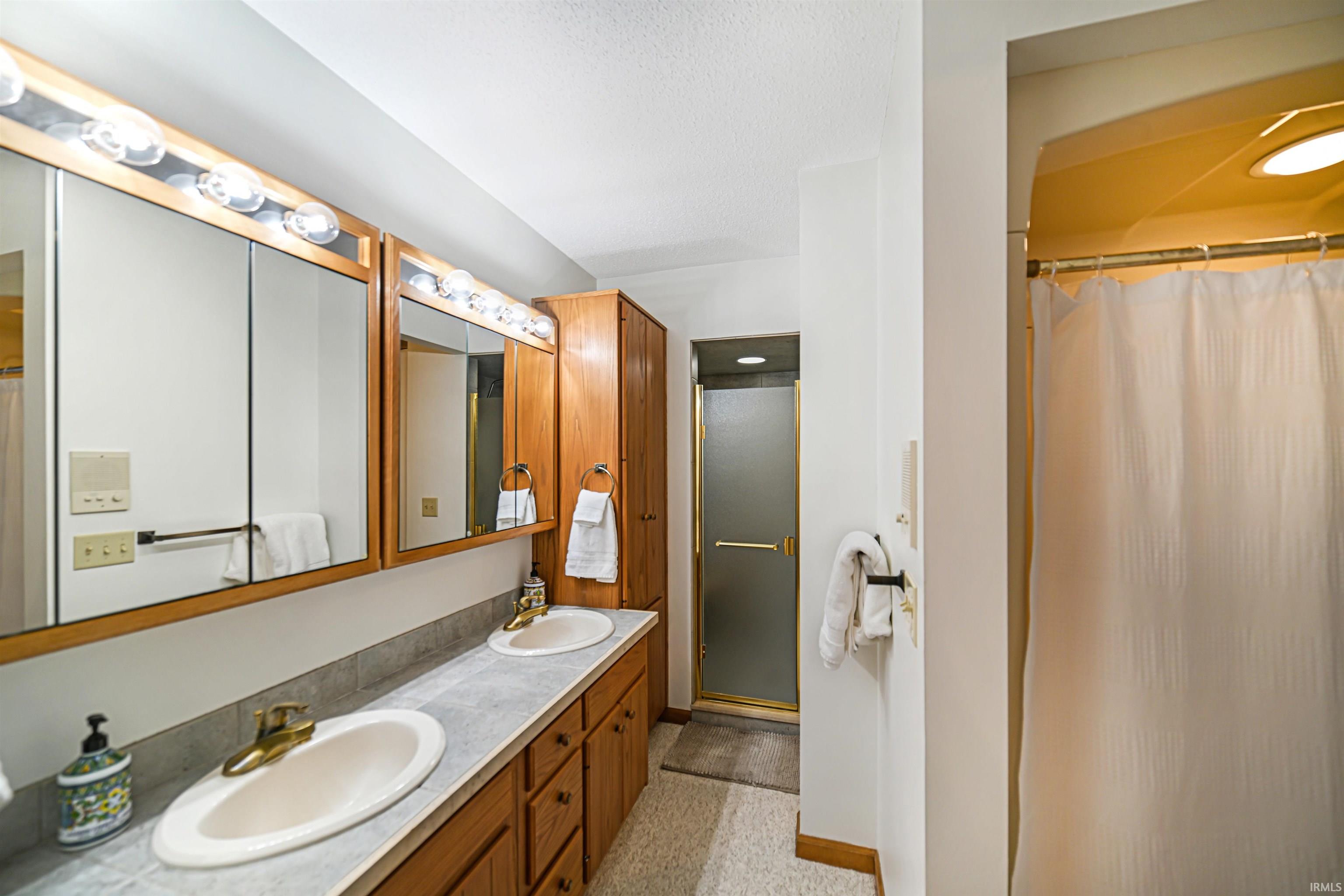 Full bathroom featuring a stall shower, double vanity, and a textured ceiling
