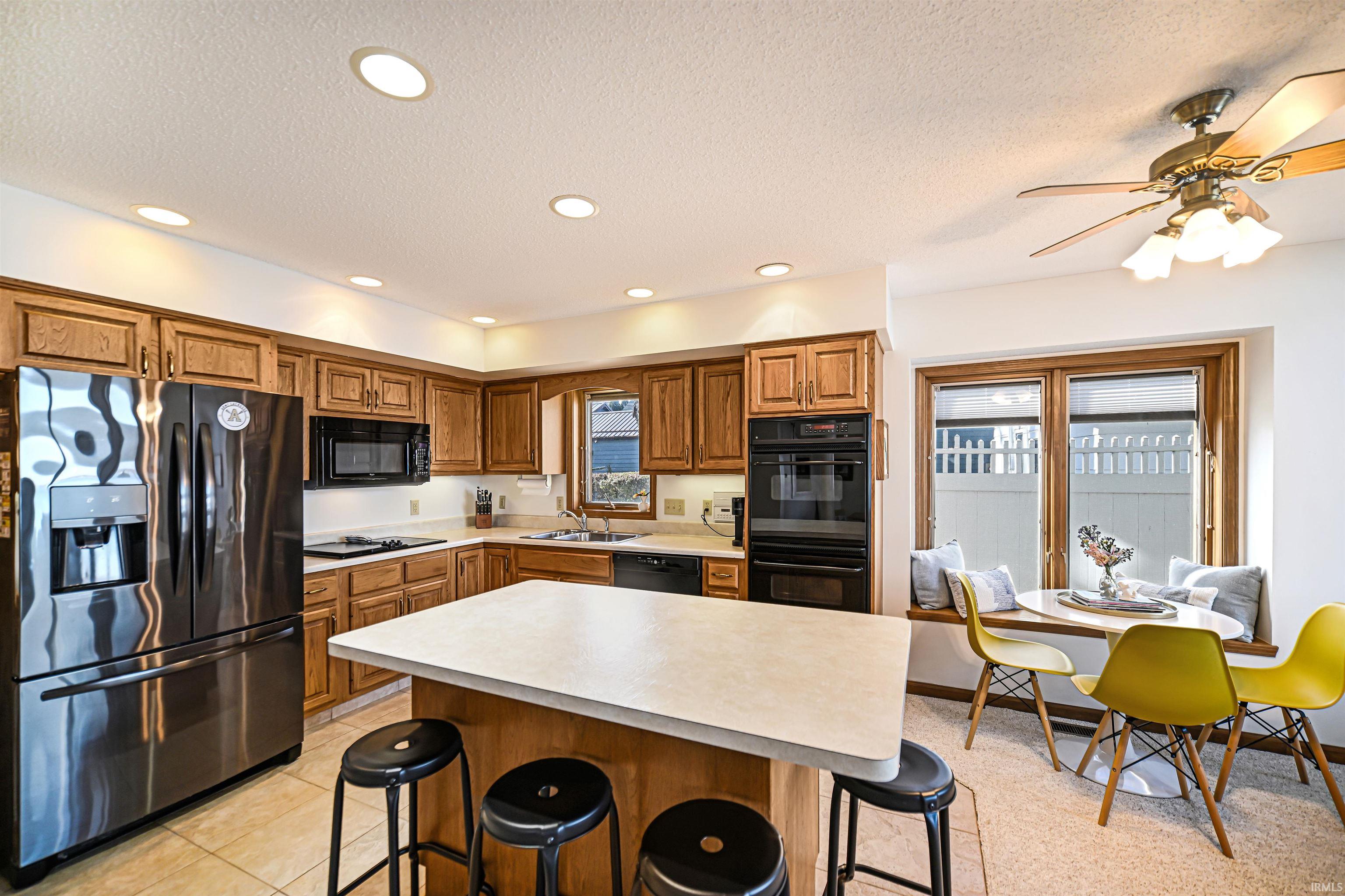 Kitchen featuring a breakfast bar, black appliances, brown cabinetry, recessed lighting, and a textured ceiling