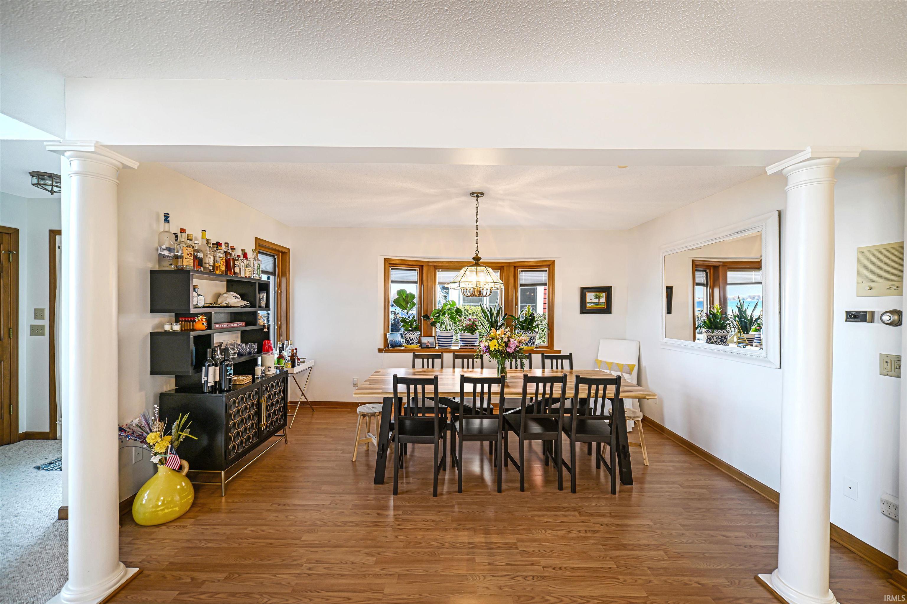 Dining space with ornate columns, wood finished floors, healthy amount of natural light, and a textured ceiling