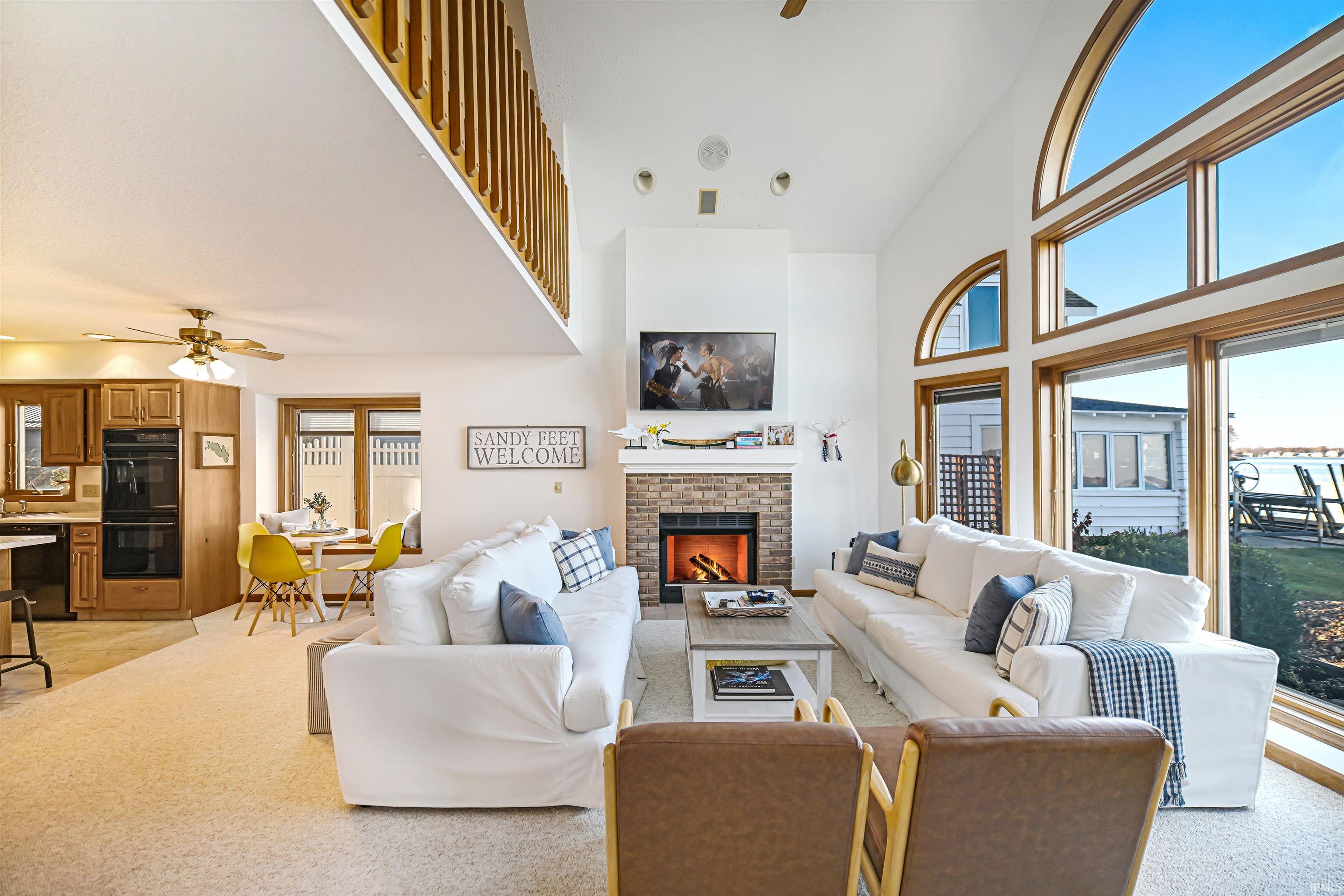 Living area with ceiling fan, plenty of natural light, a brick fireplace, and a high ceiling