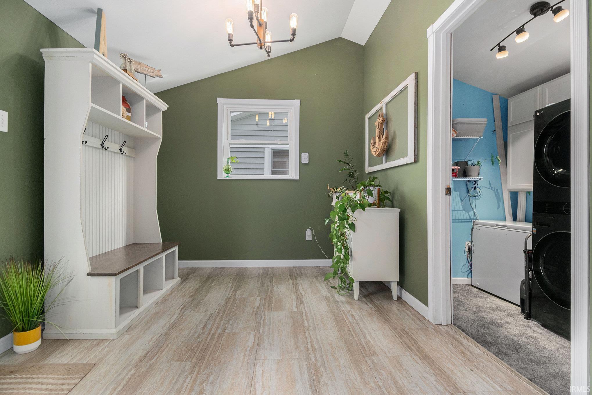 Mudroom featuring a chandelier, lofted ceiling, stacked washer / dryer, and light wood-style floors