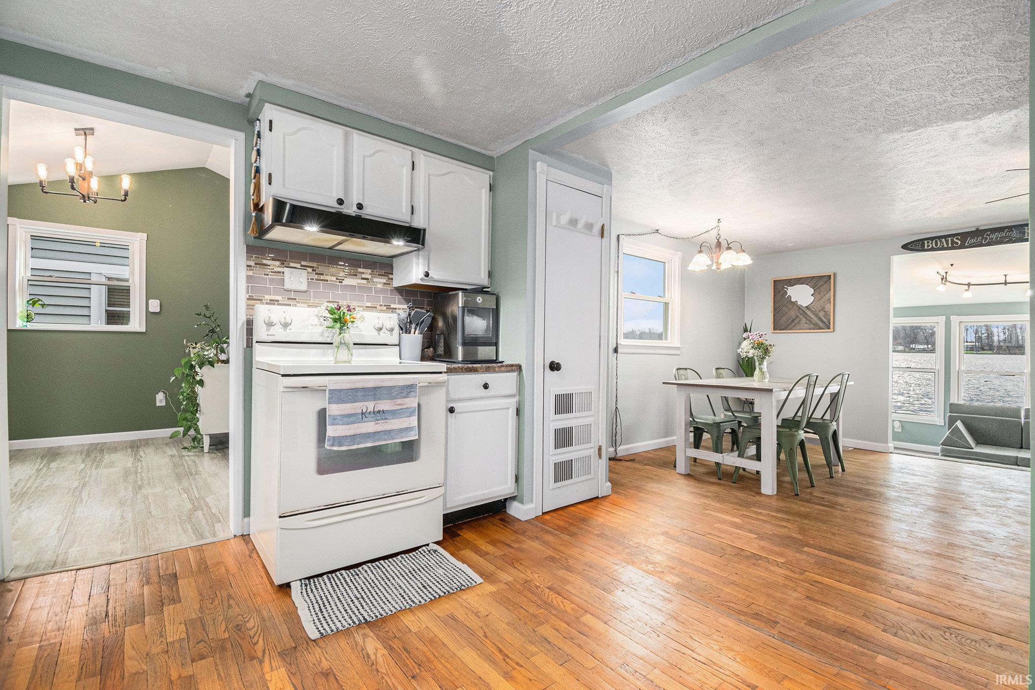 Kitchen with a chandelier, white range with electric stovetop, hanging light fixtures, white cabinetry, and a textured ceiling