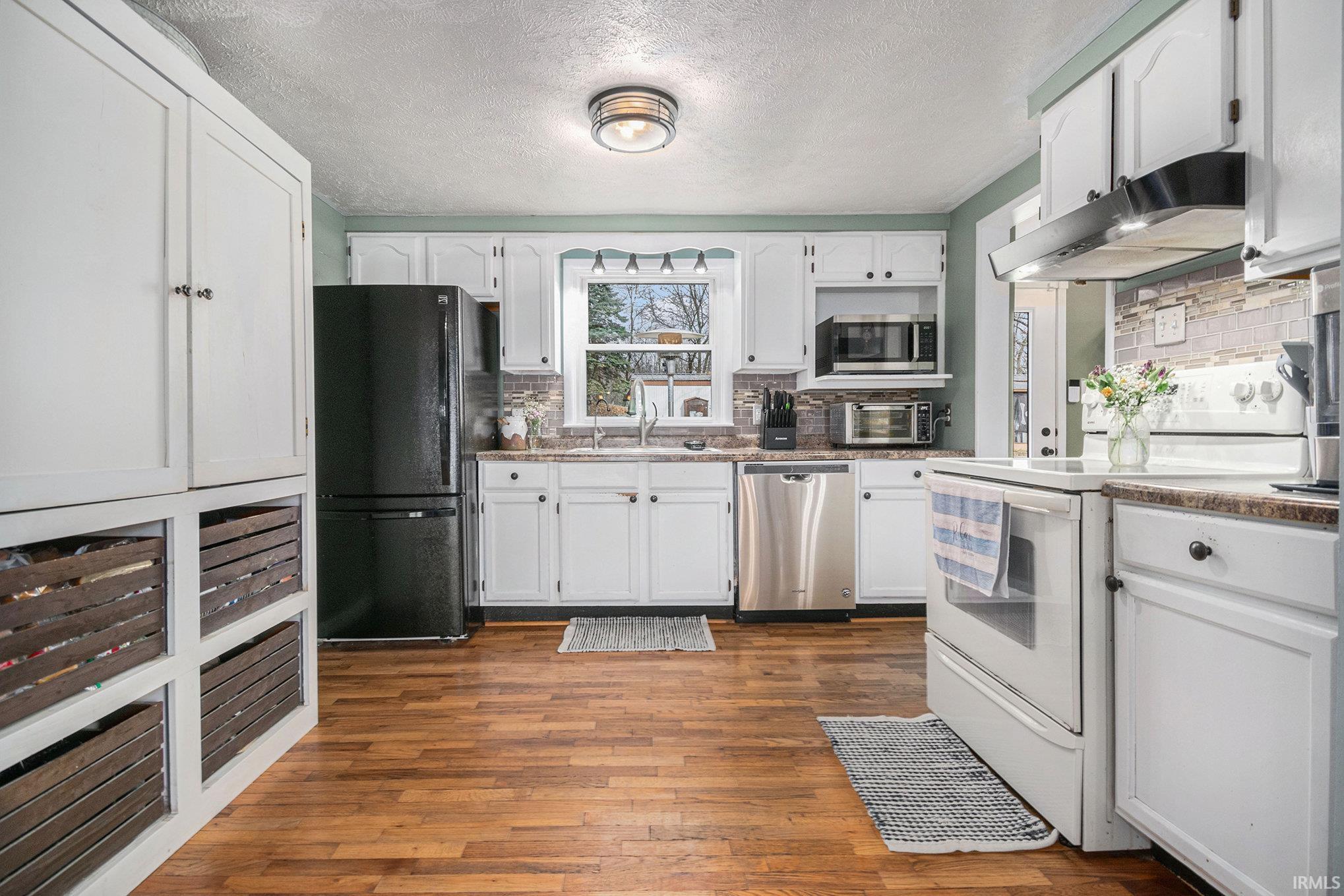 Kitchen with stainless steel appliances, white cabinetry, a textured ceiling, under cabinet range hood, and backsplash