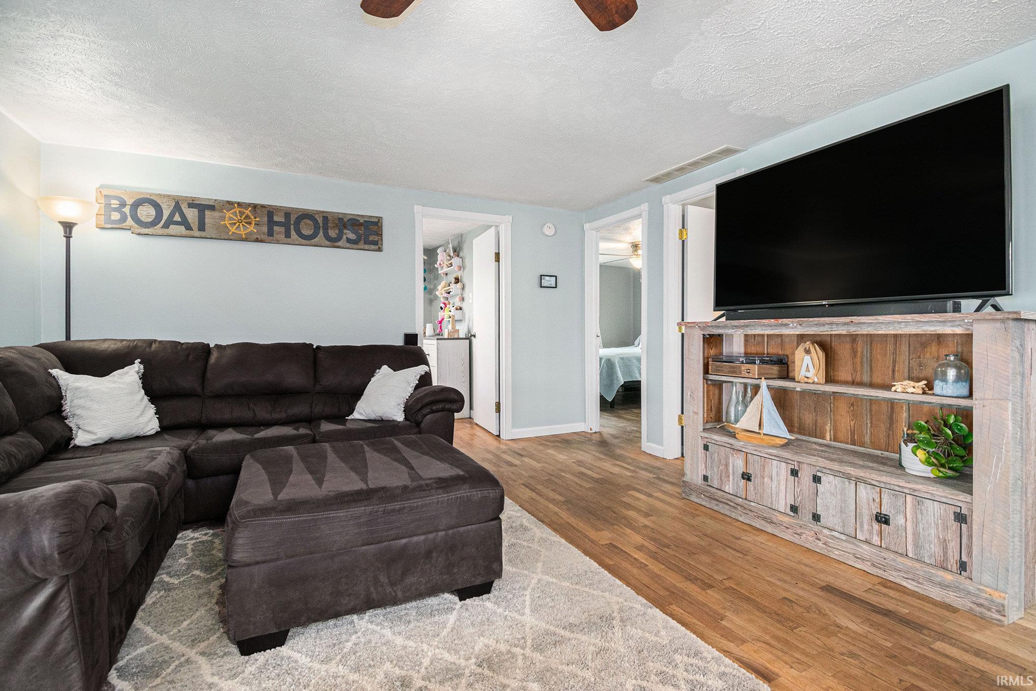 Living area with a textured ceiling, wood finished floors, and a ceiling fan
