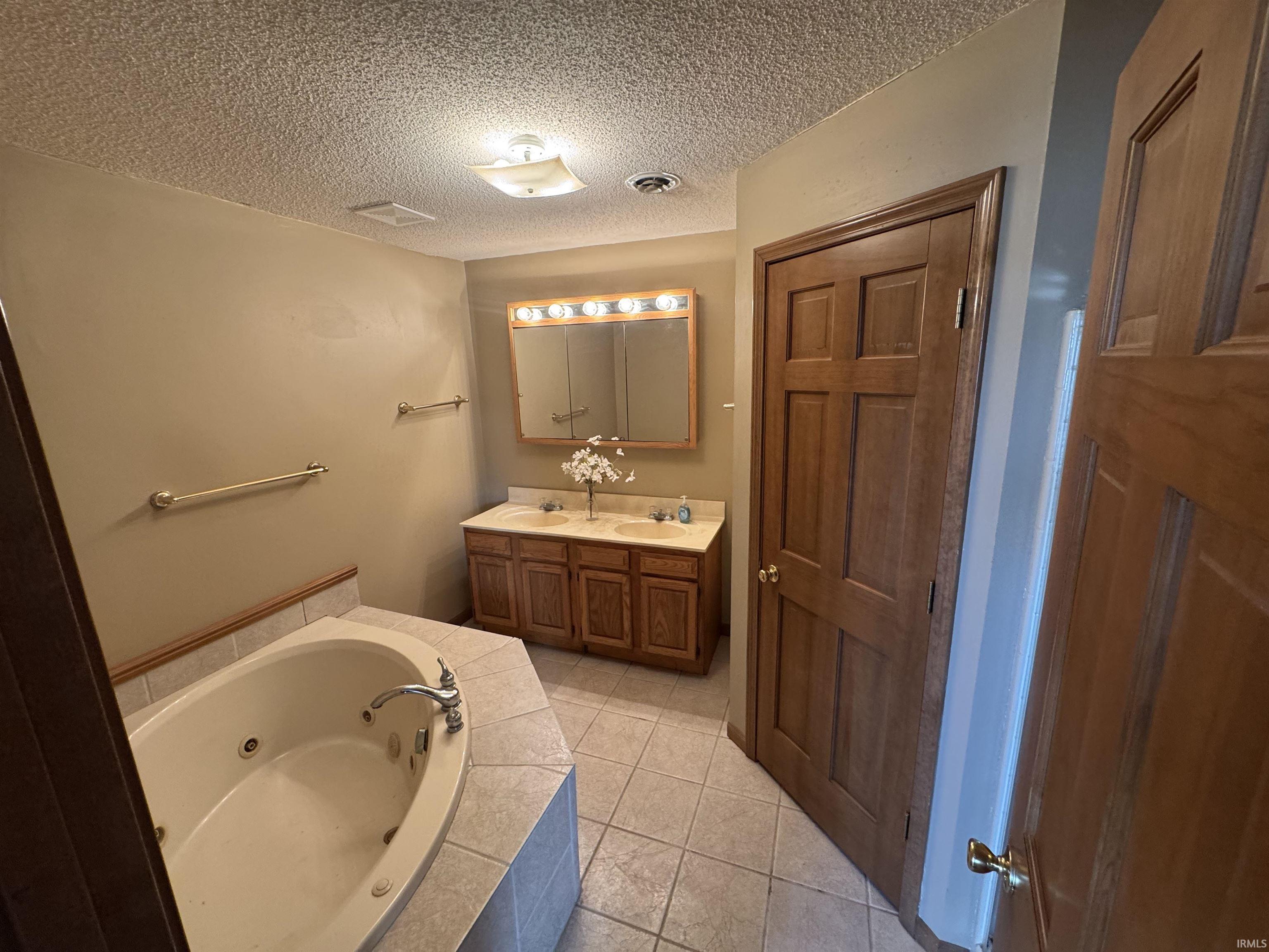Bathroom featuring double vanity, a whirlpool tub, light tile patterned floors, and a textured ceiling