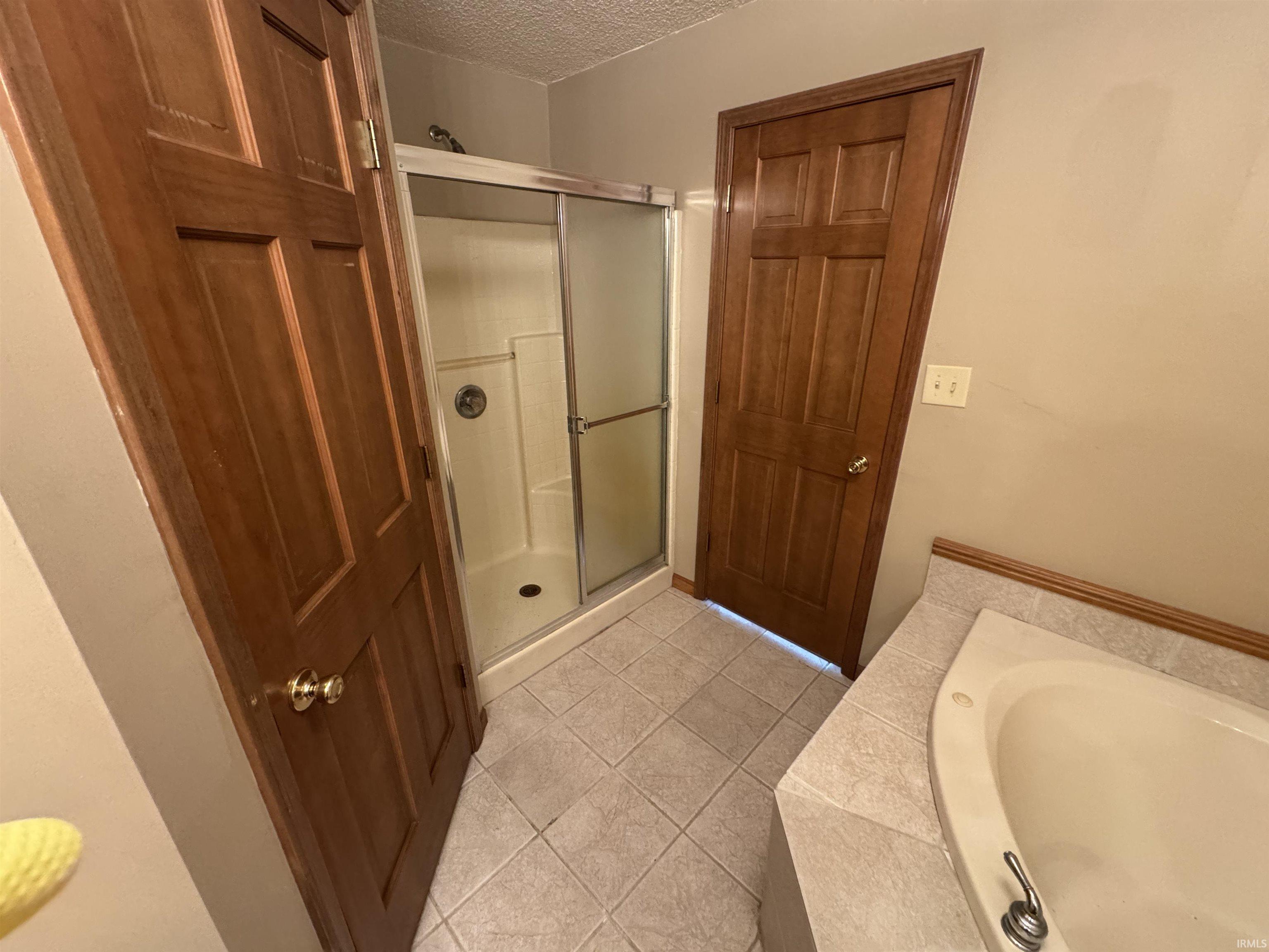 Full bath featuring a shower stall, light tile patterned flooring, tiled bath, and a textured ceiling