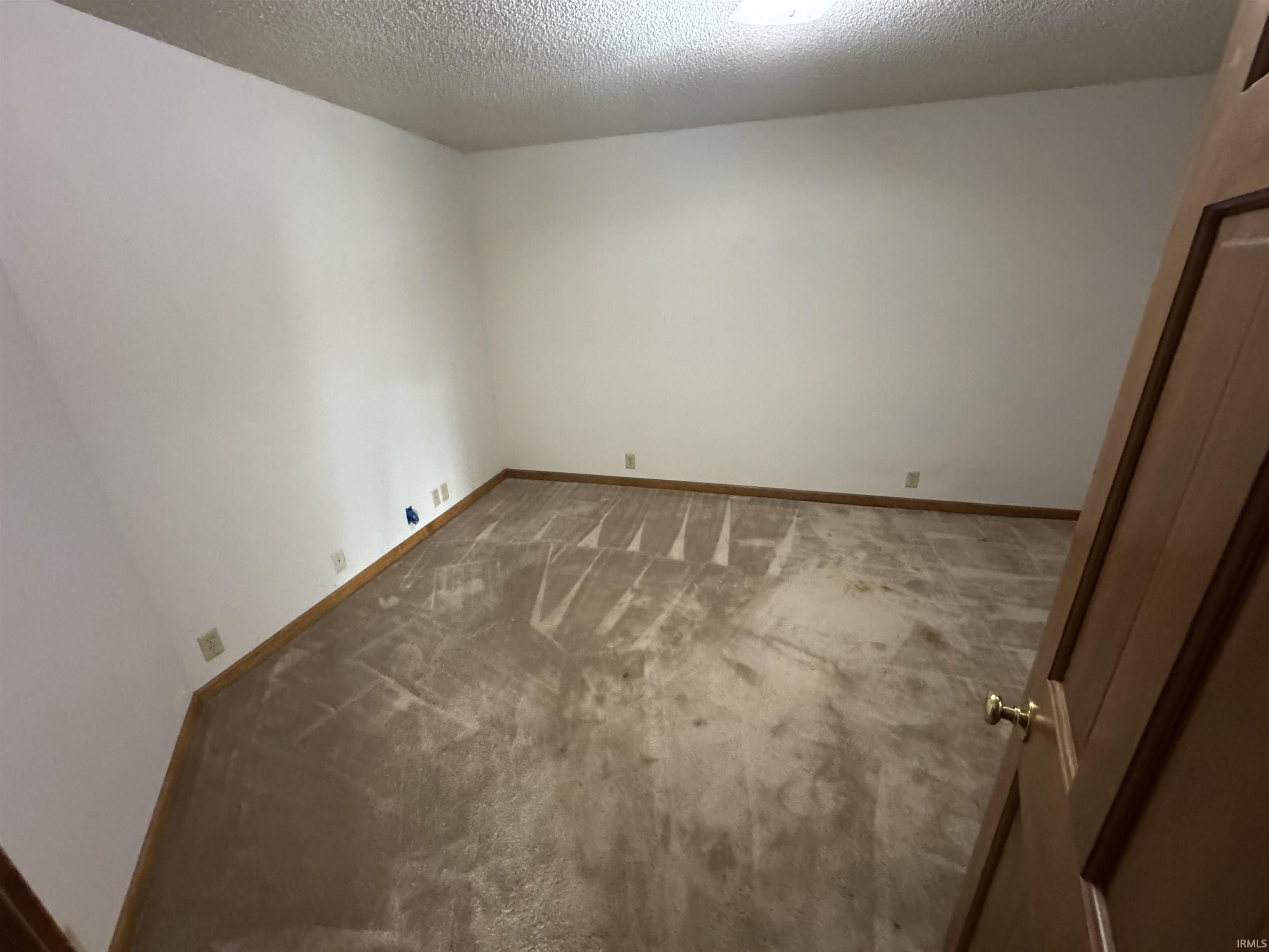 Carpeted spare room featuring a textured ceiling and baseboards
