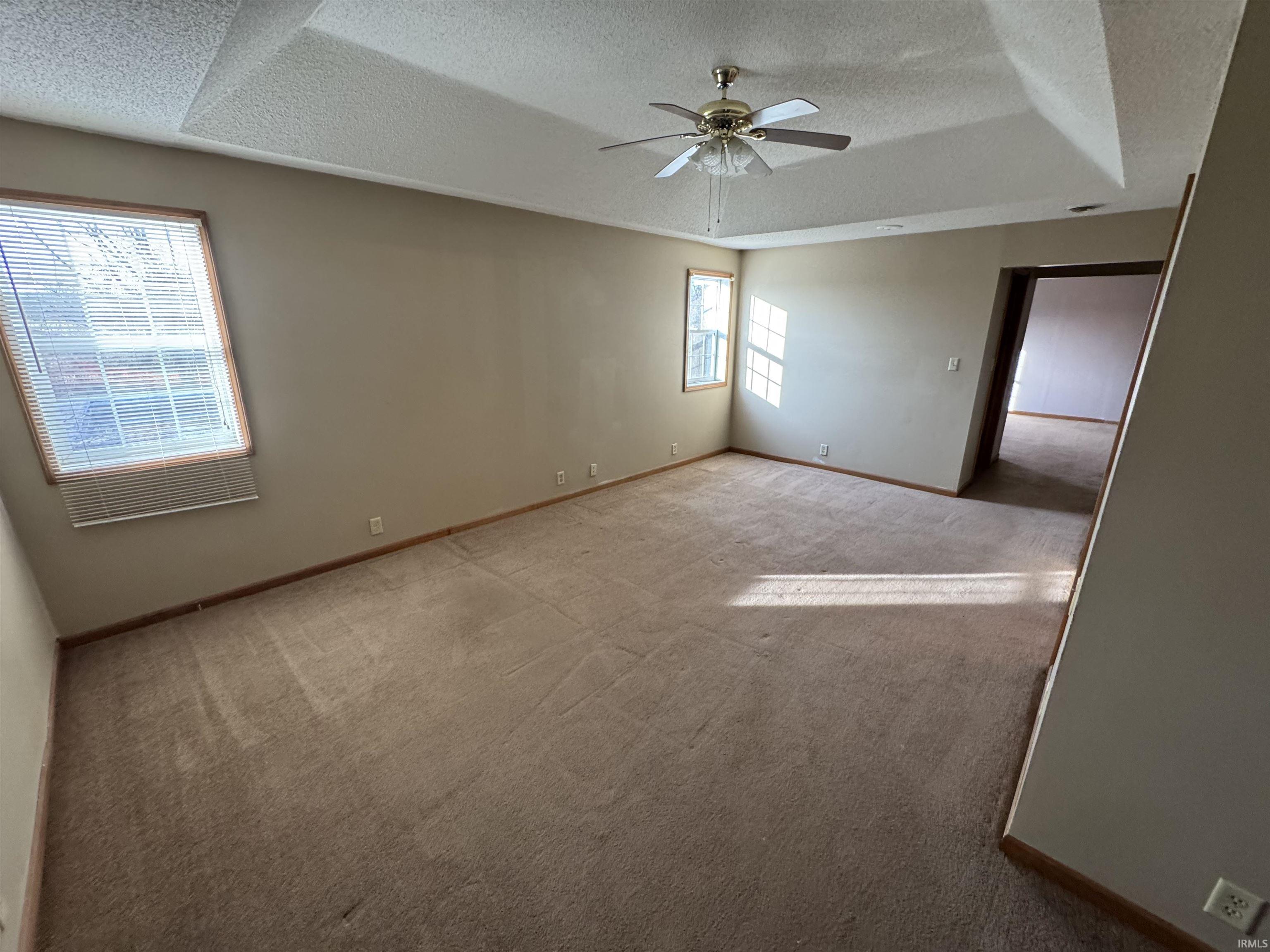 Empty room with a textured ceiling, carpet, ceiling fan, and a tray ceiling