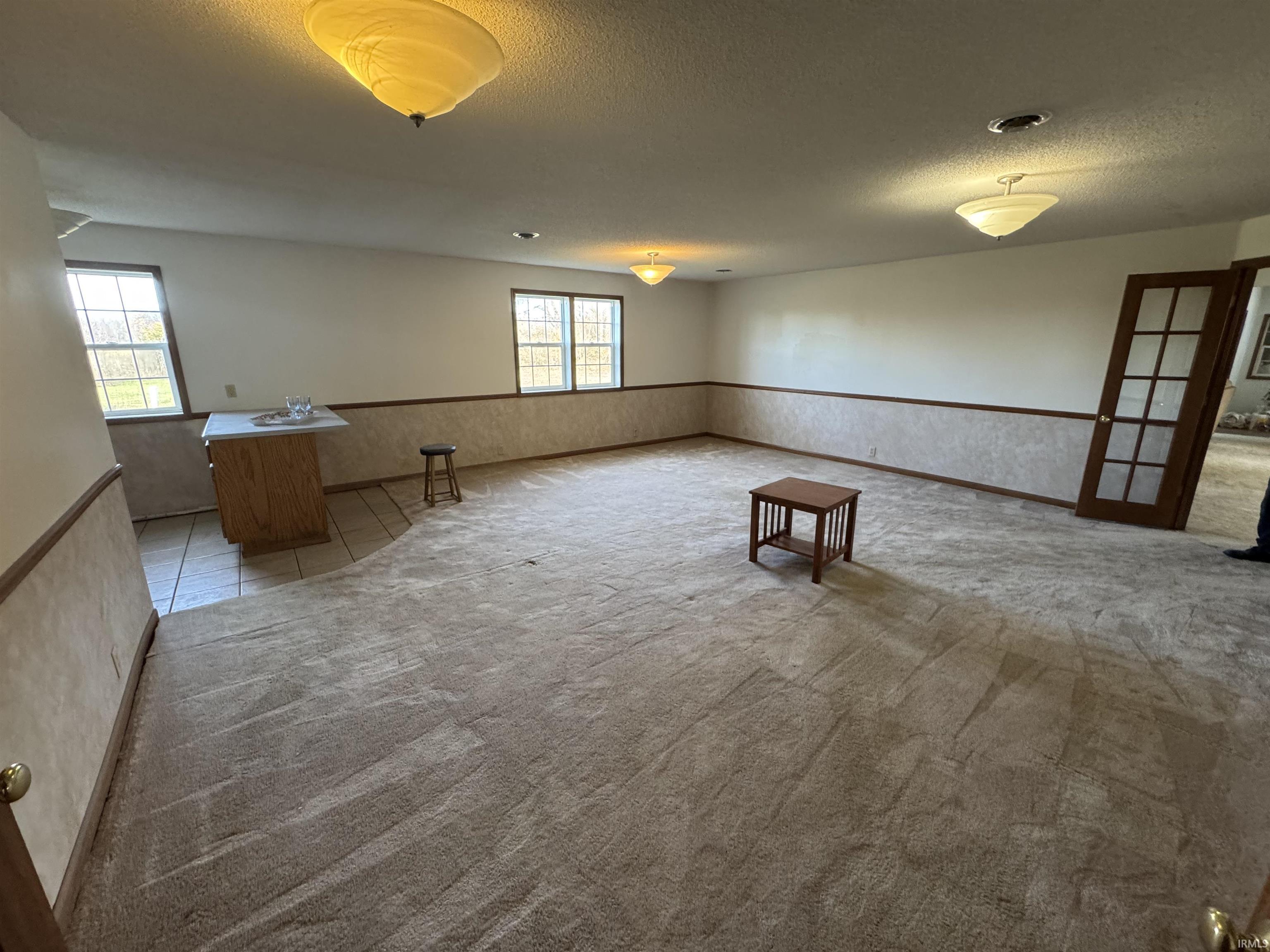 Unfurnished room featuring a wainscoted wall, a textured ceiling, light carpet, and light tile patterned floors