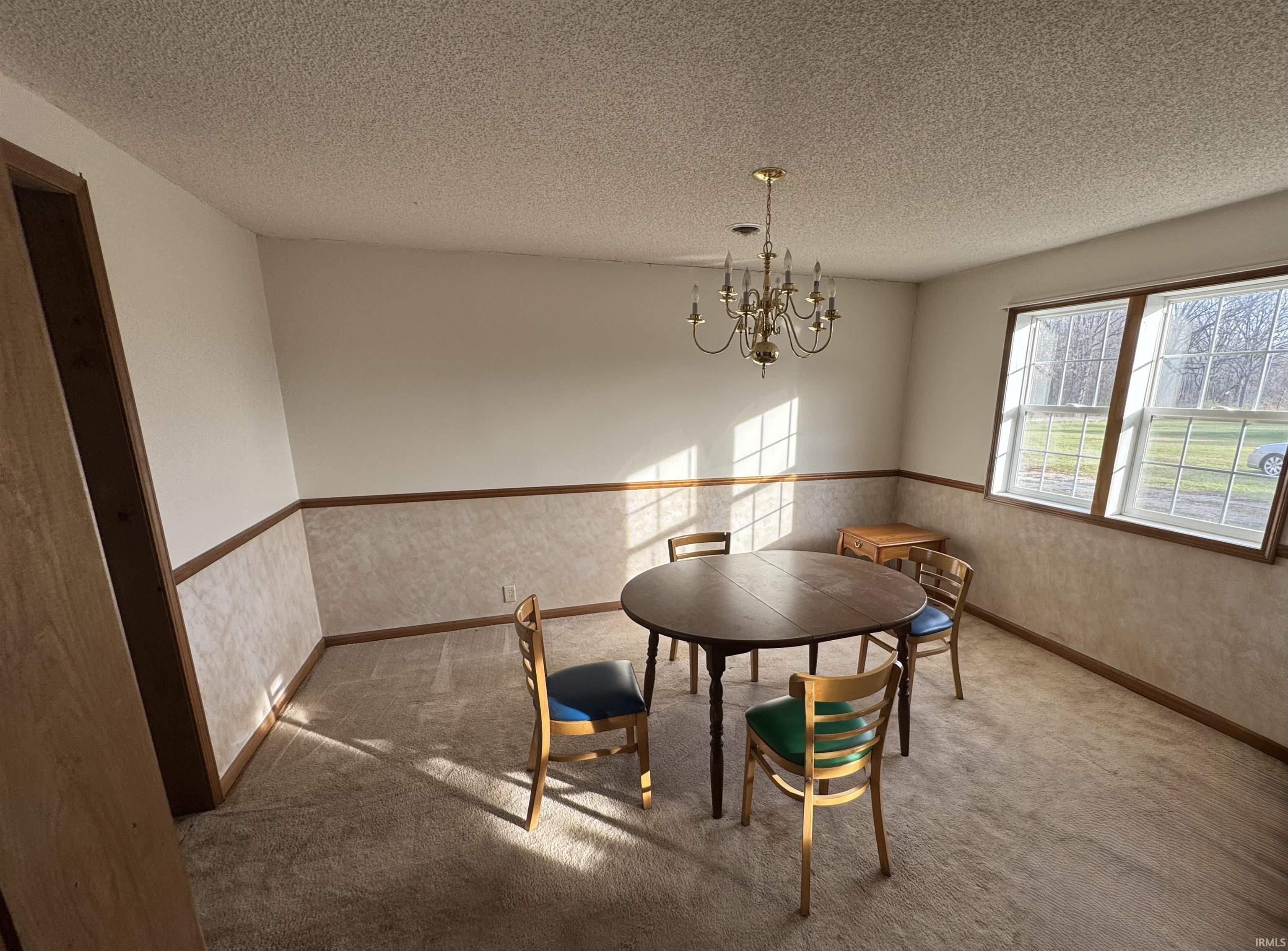 Carpeted dining room featuring a textured ceiling, a chandelier, and a wainscoted wall