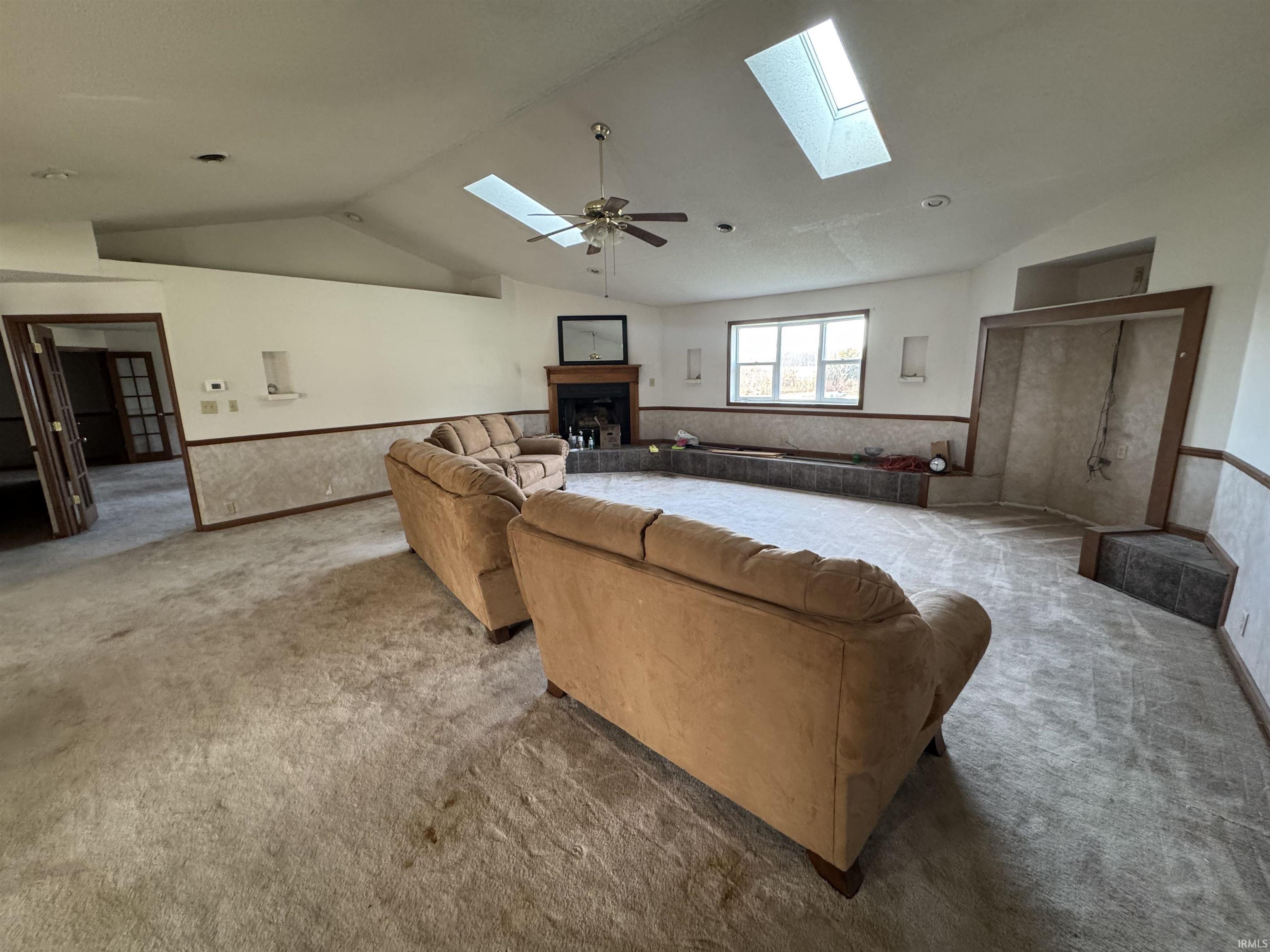 Carpeted living area featuring lofted ceiling, a fireplace with raised hearth, a skylight, and a ceiling fan