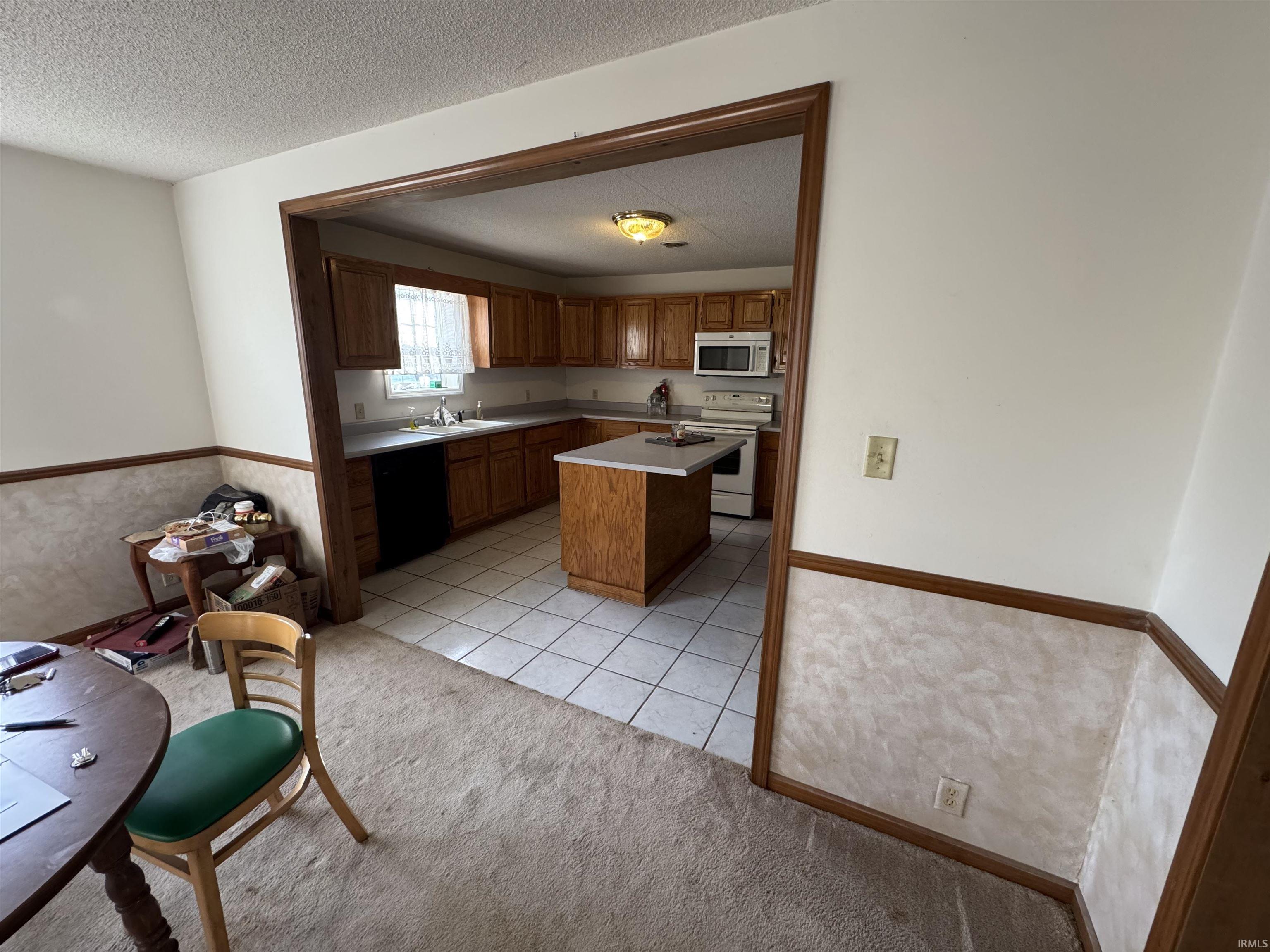 Kitchen with electric range, a textured ceiling, a kitchen island, brown cabinets, and light colored carpet