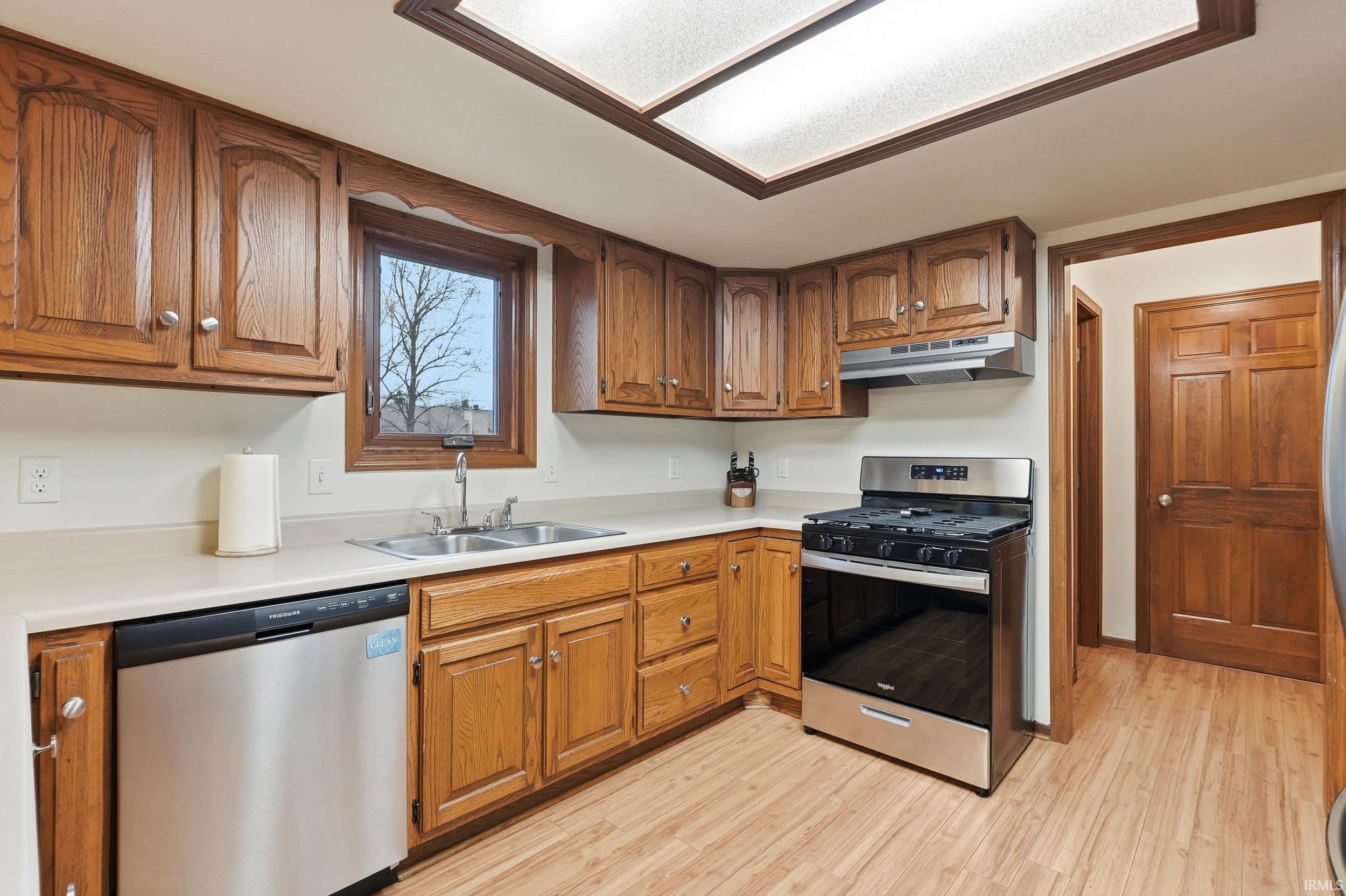 Kitchen featuring stainless steel appliances, brown cabinets, light countertops, under cabinet range hood, and light wood-style floors