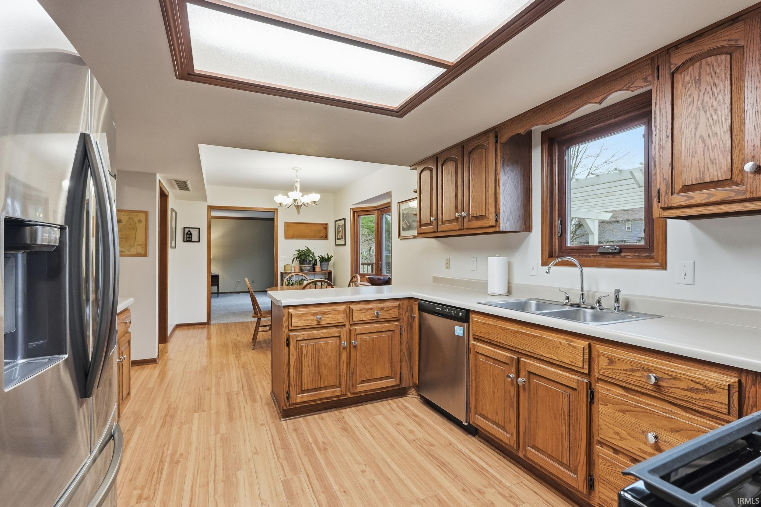 Kitchen with a chandelier, appliances with stainless steel finishes, a peninsula, light countertops, and brown cabinets