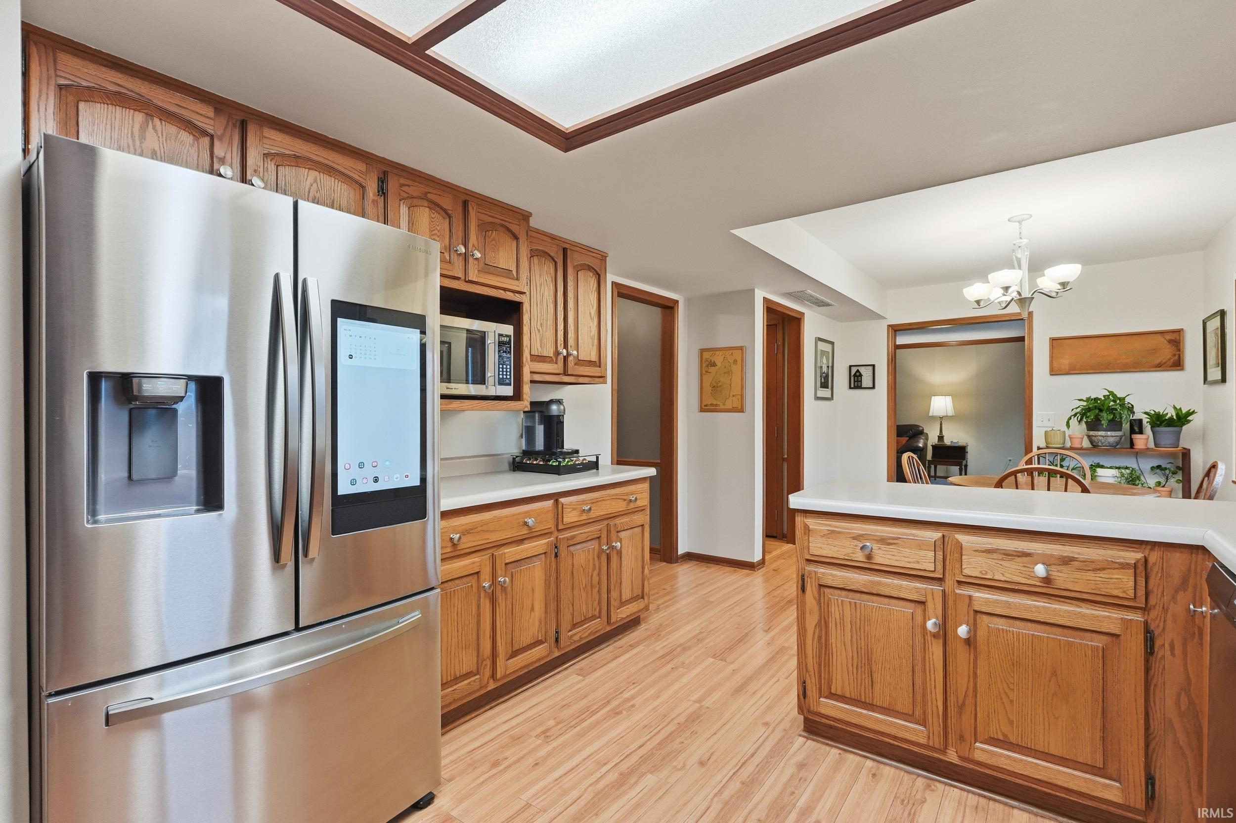 Kitchen featuring appliances with stainless steel finishes, brown cabinets, light countertops, a chandelier, and decorative light fixtures