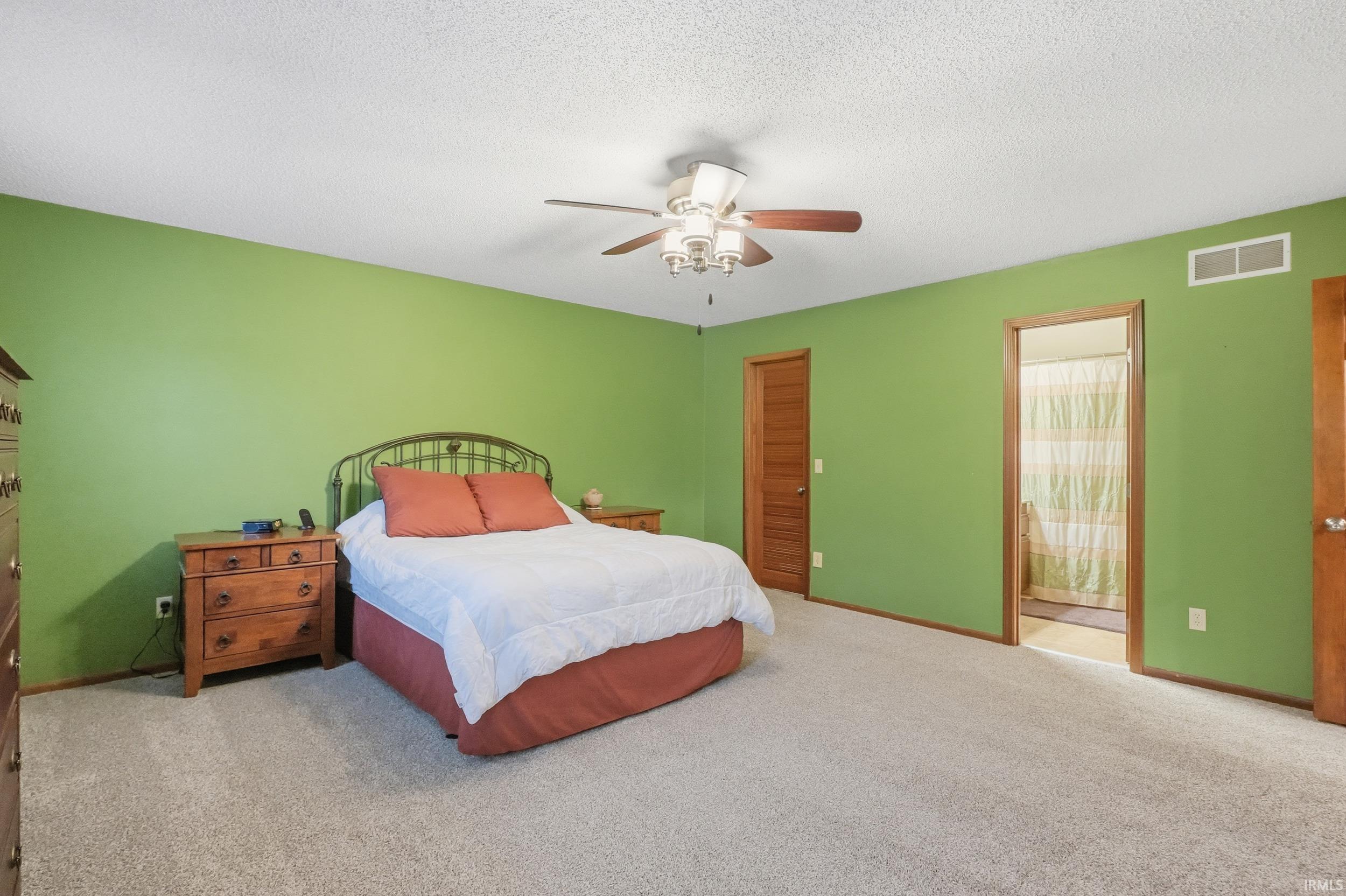 Bedroom with a textured ceiling, carpet, a closet, a ceiling fan, and connected bathroom