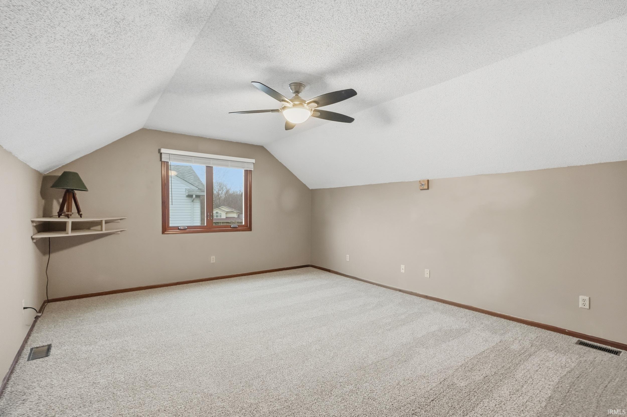 Additional living space with vaulted ceiling, carpet flooring, ceiling fan, and a textured ceiling