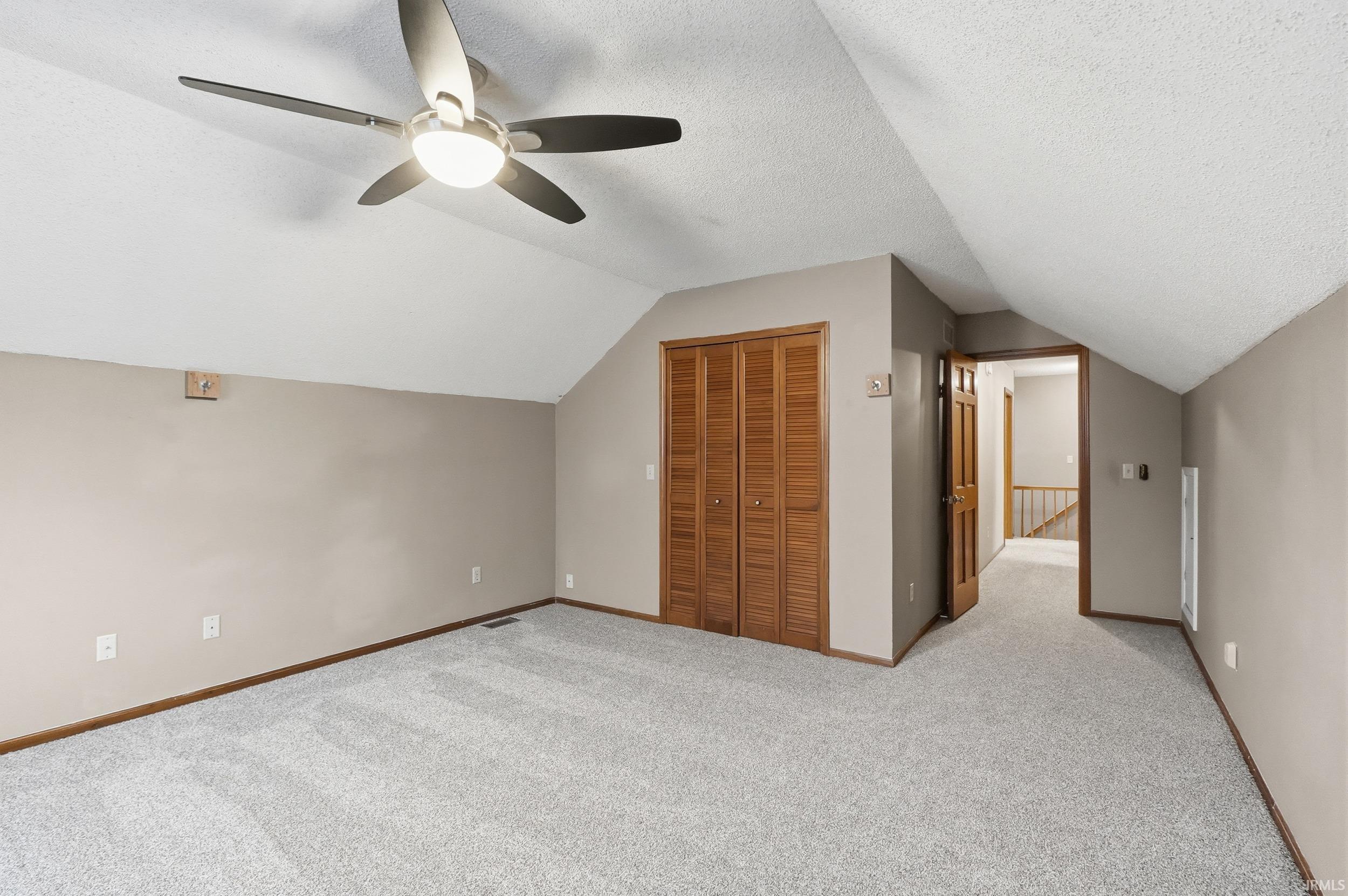 Bonus room with carpet flooring, vaulted ceiling, a ceiling fan, and a textured ceiling