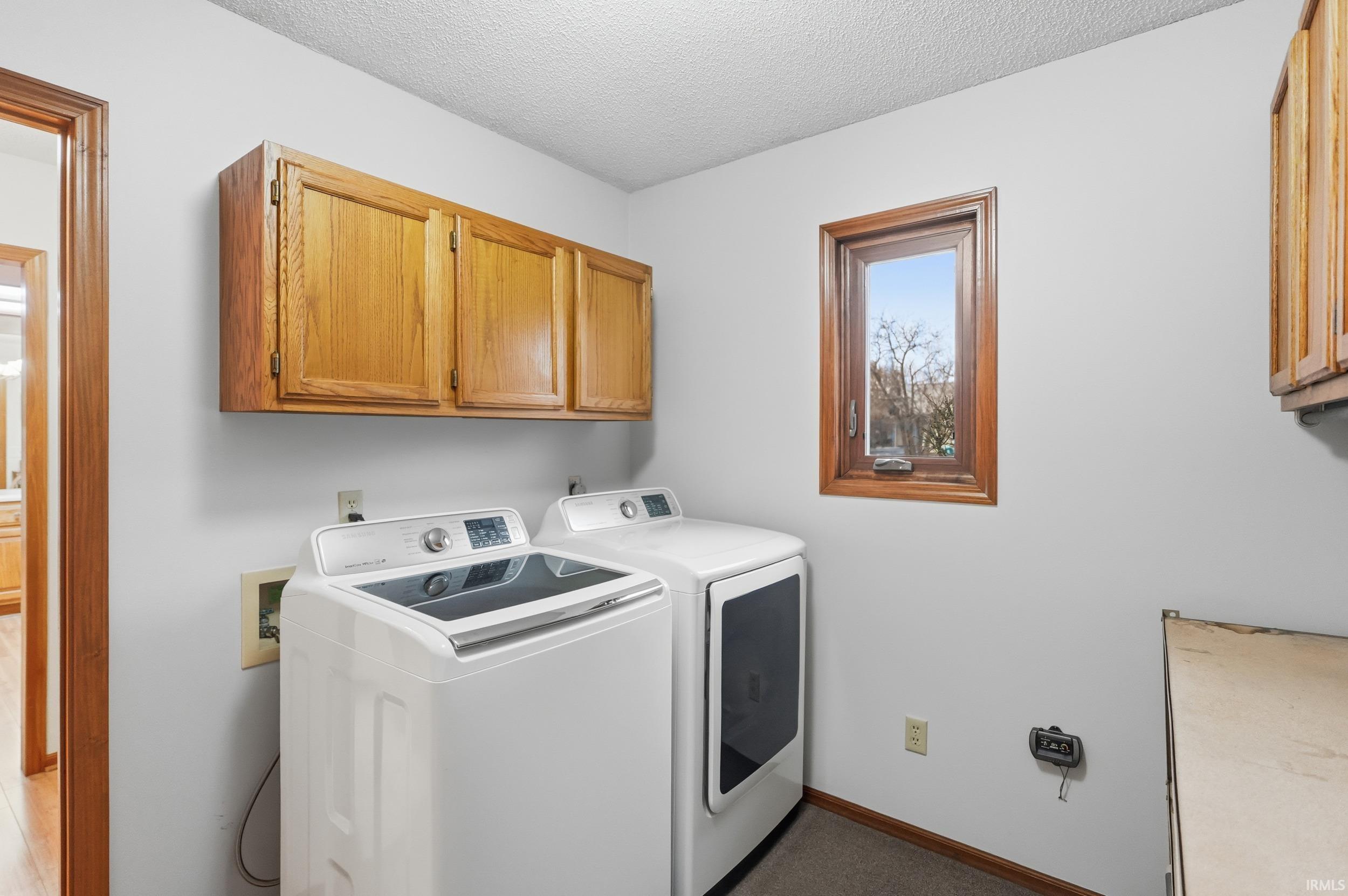 Laundry room featuring cabinet space, a textured ceiling, and separate washer and dryer