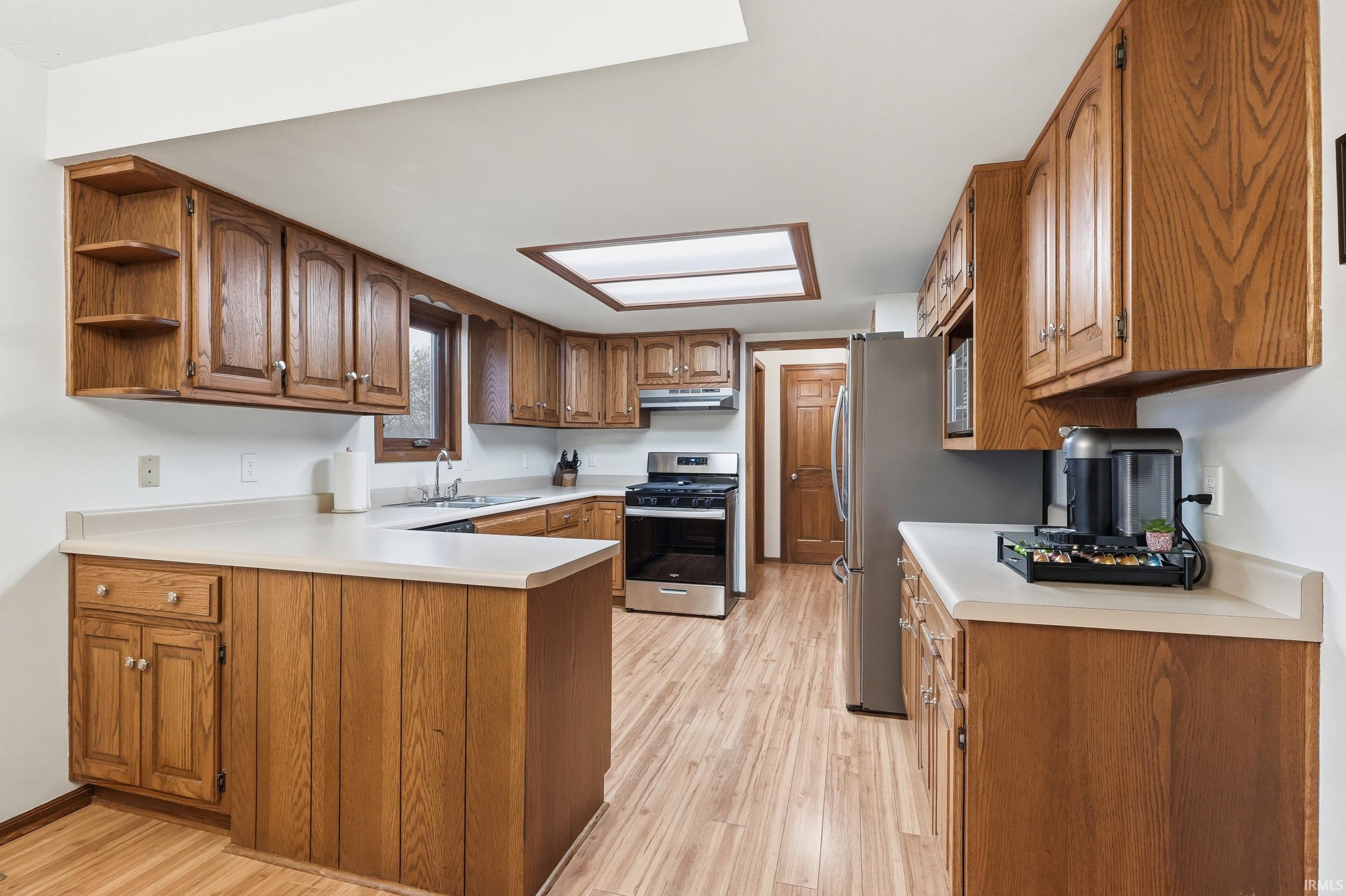 Kitchen with brown cabinetry, light countertops, stainless steel appliances, a peninsula, and open shelves