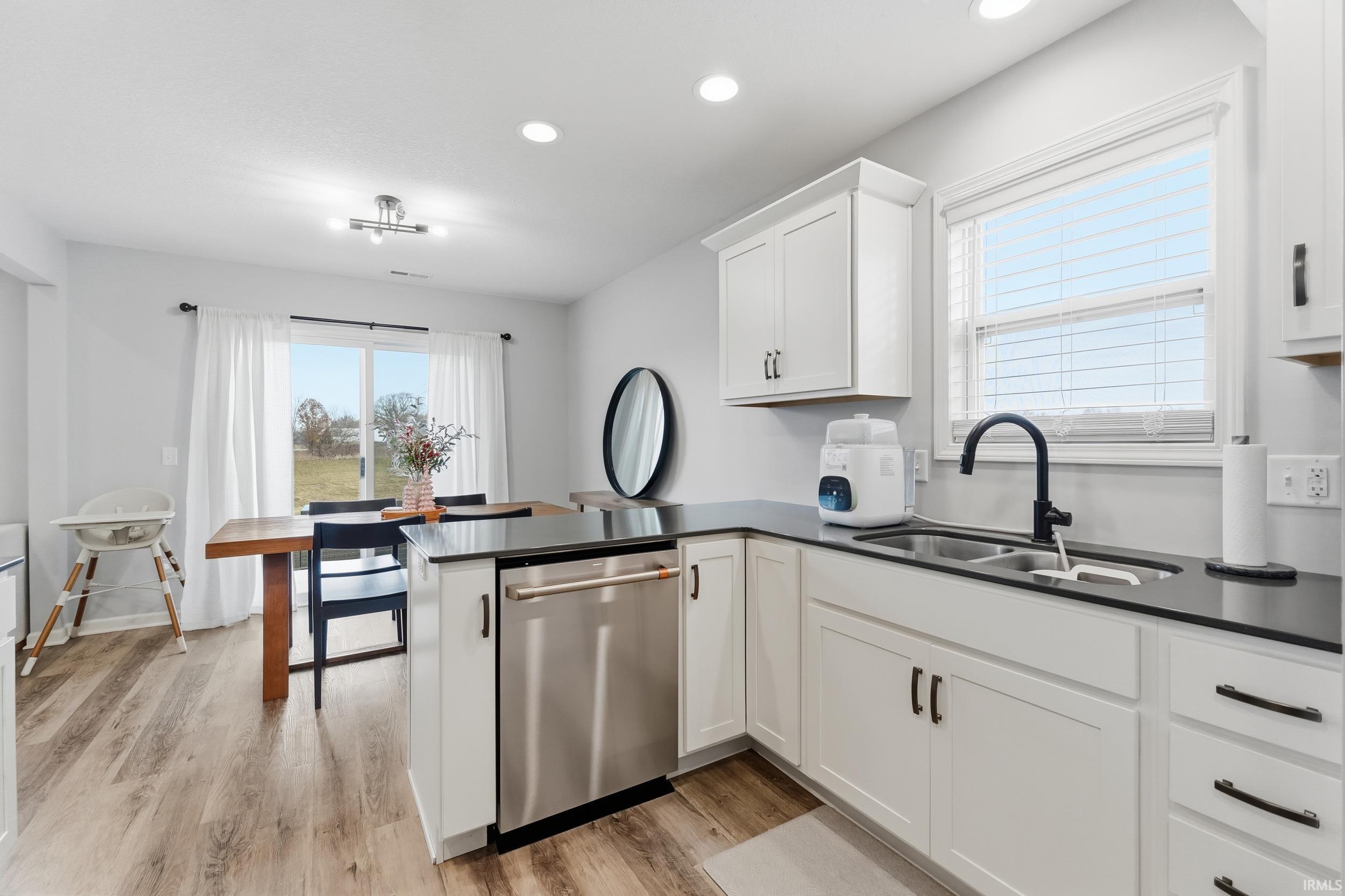 Kitchen with a peninsula, white cabinets, stainless steel dishwasher, light wood-type flooring, and recessed lighting