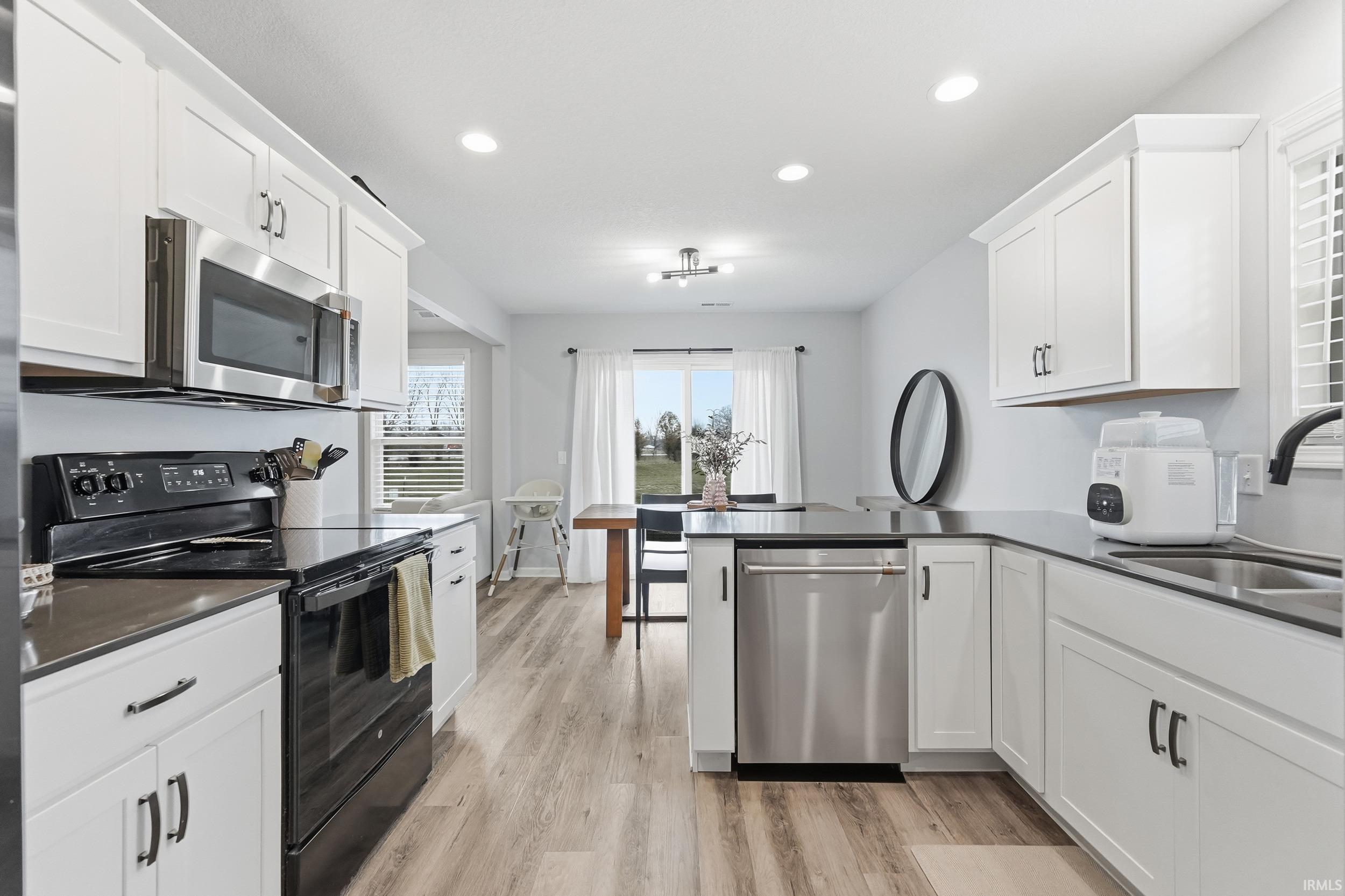 Kitchen featuring stainless steel appliances, a peninsula, white cabinetry, light wood-style flooring, and recessed lighting