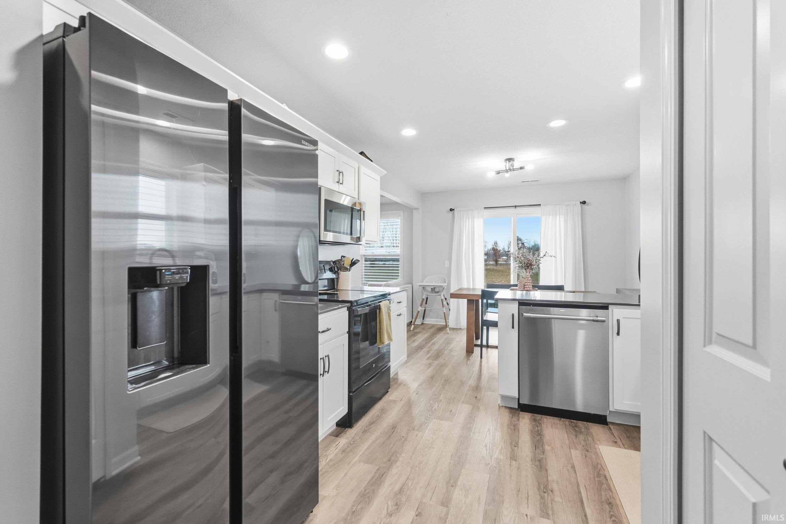 Kitchen with appliances with stainless steel finishes, dark countertops, white cabinets, light wood finished floors, and recessed lighting