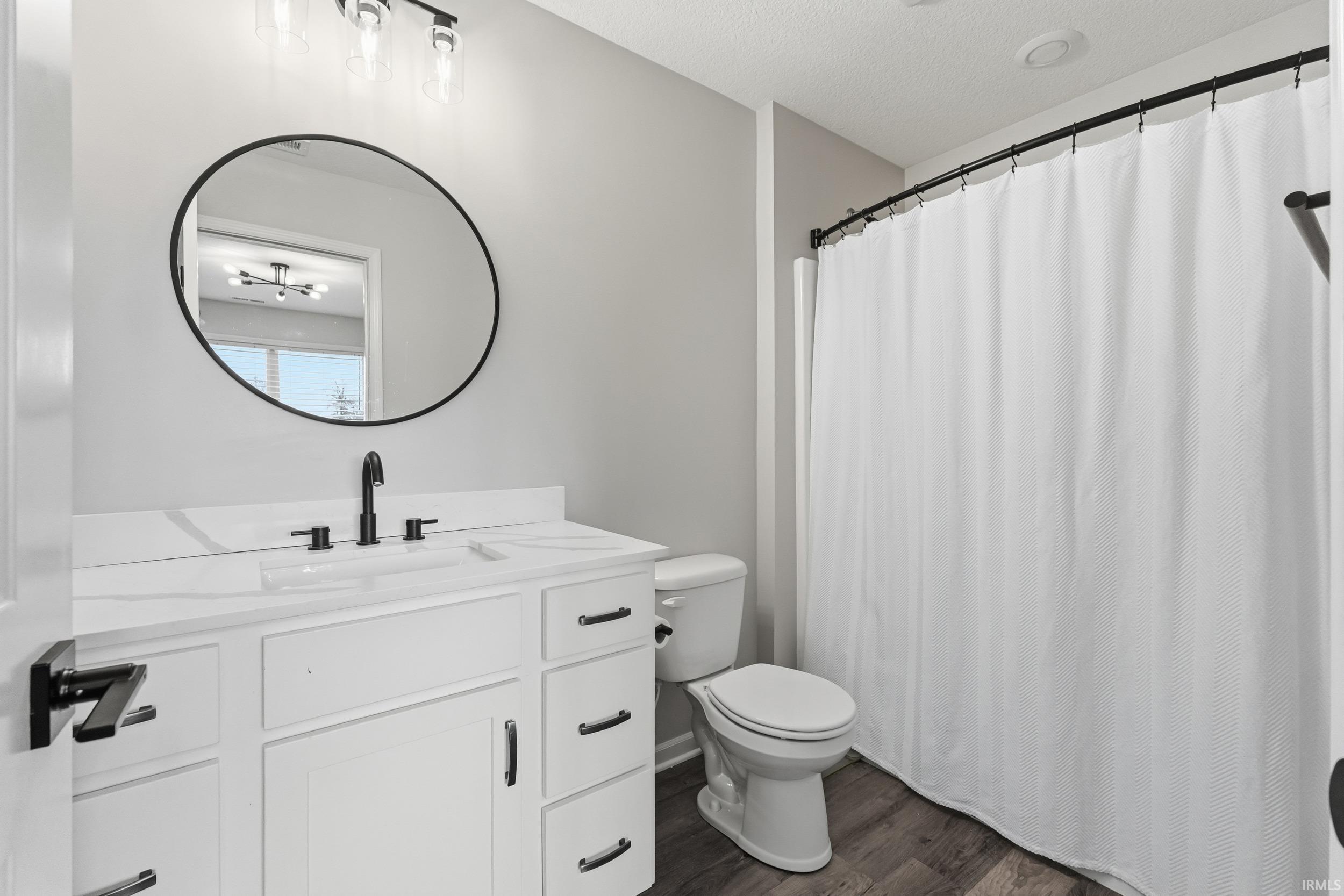 Full bath featuring a shower with shower curtain, vanity, dark wood-style floors, and a textured ceiling