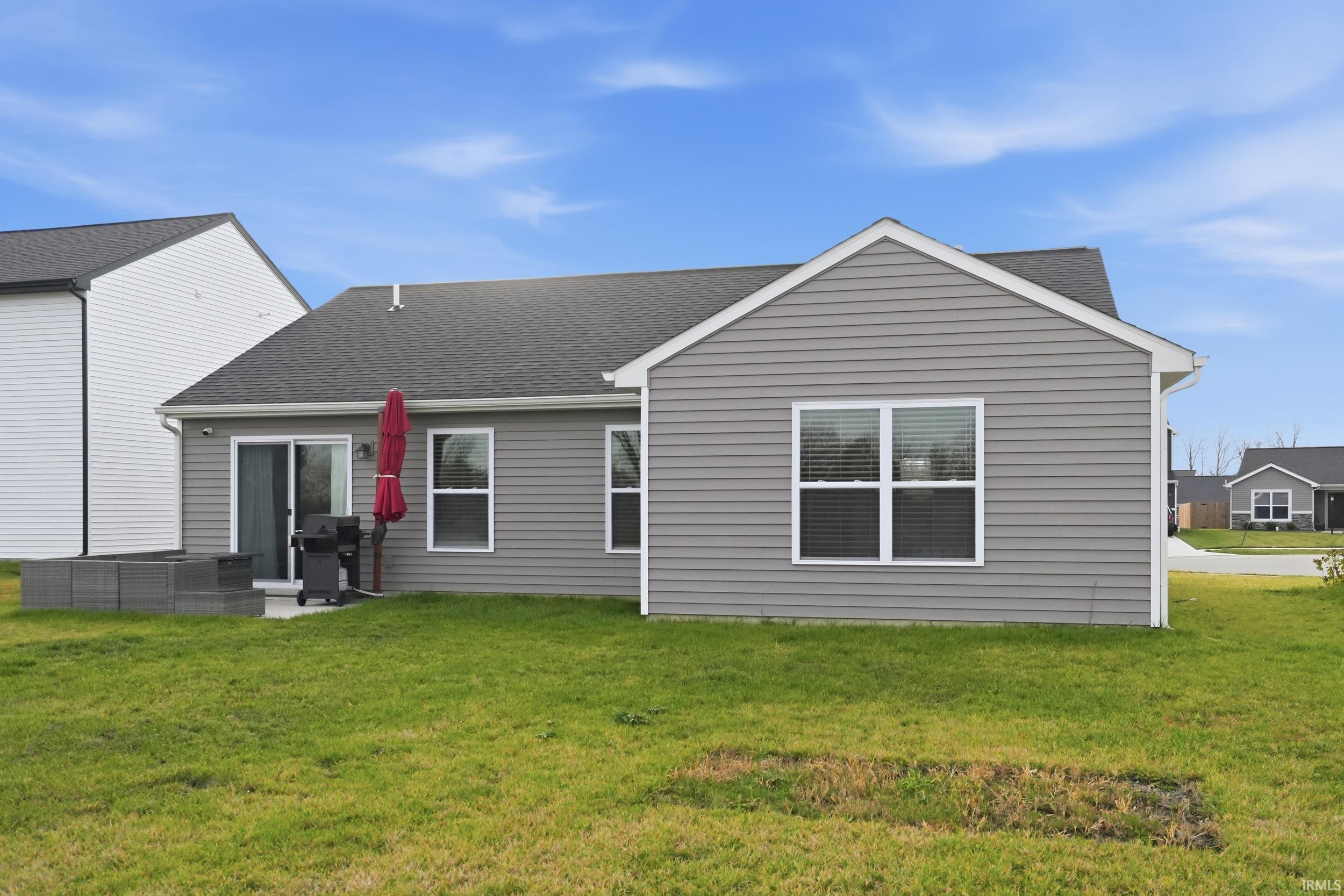 Back of property featuring a shingled roof, a lawn, and a patio