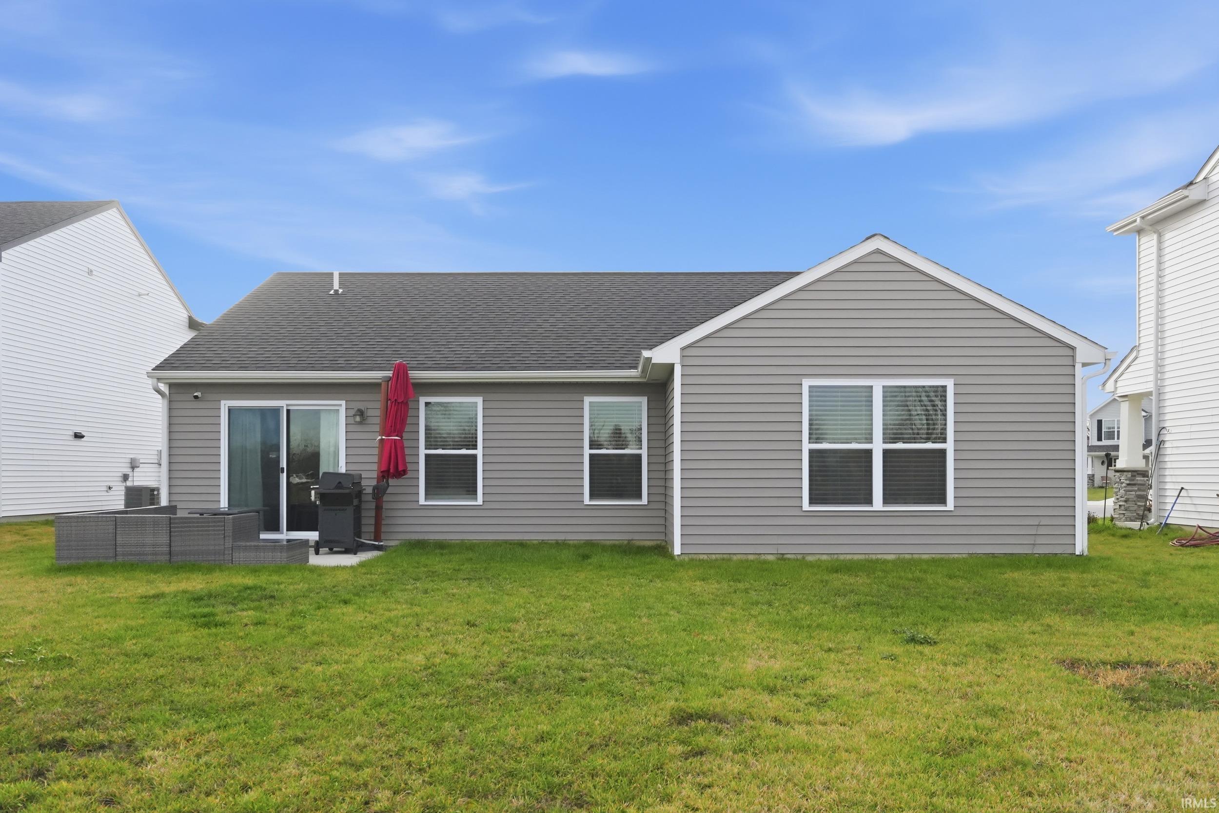 Back of house featuring a shingled roof, a yard, and a patio