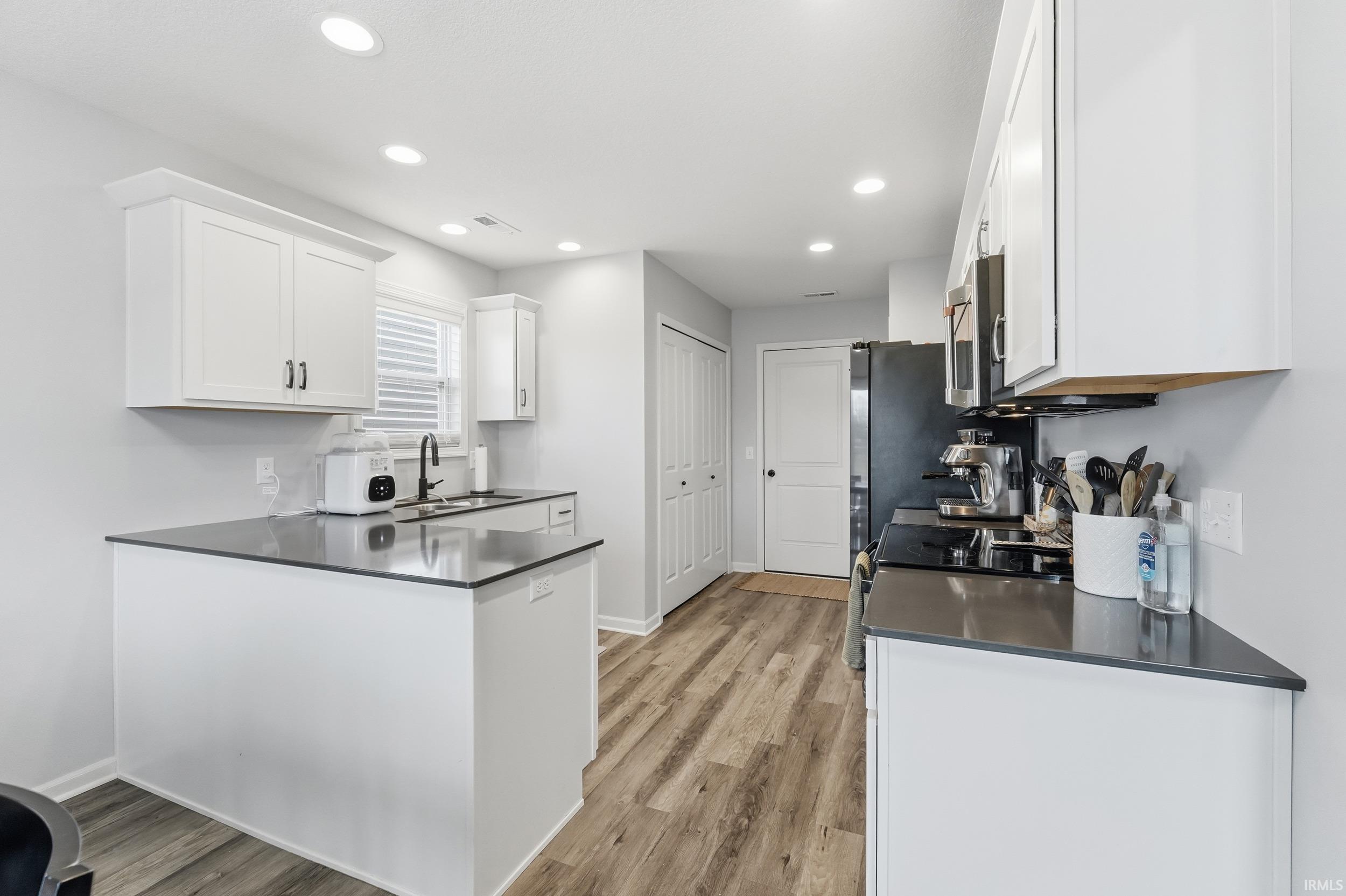 Kitchen featuring a peninsula, white cabinetry, light wood-style floors, recessed lighting, and range